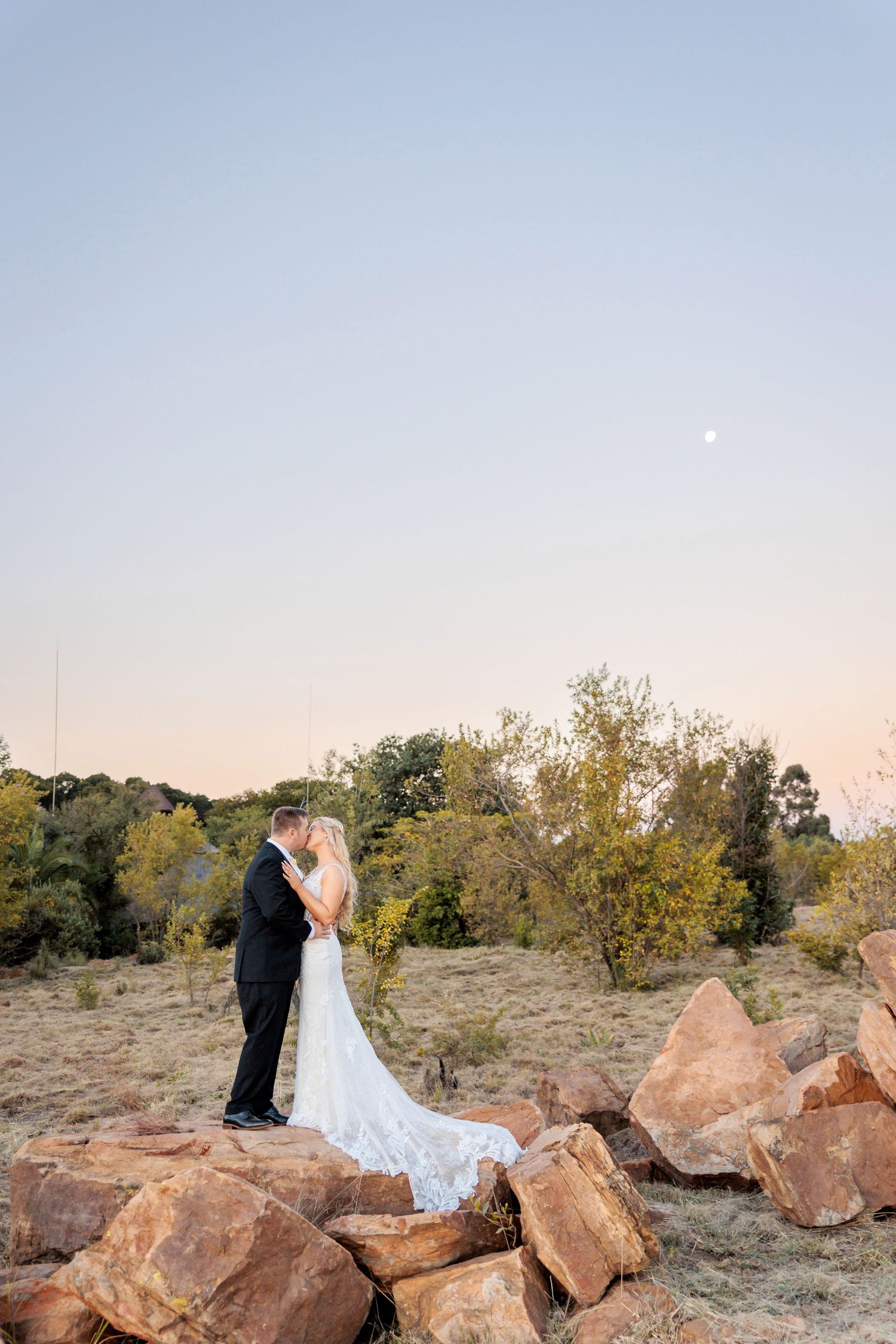Wedding couple posing on rocky terrain against clear sky at dusk.