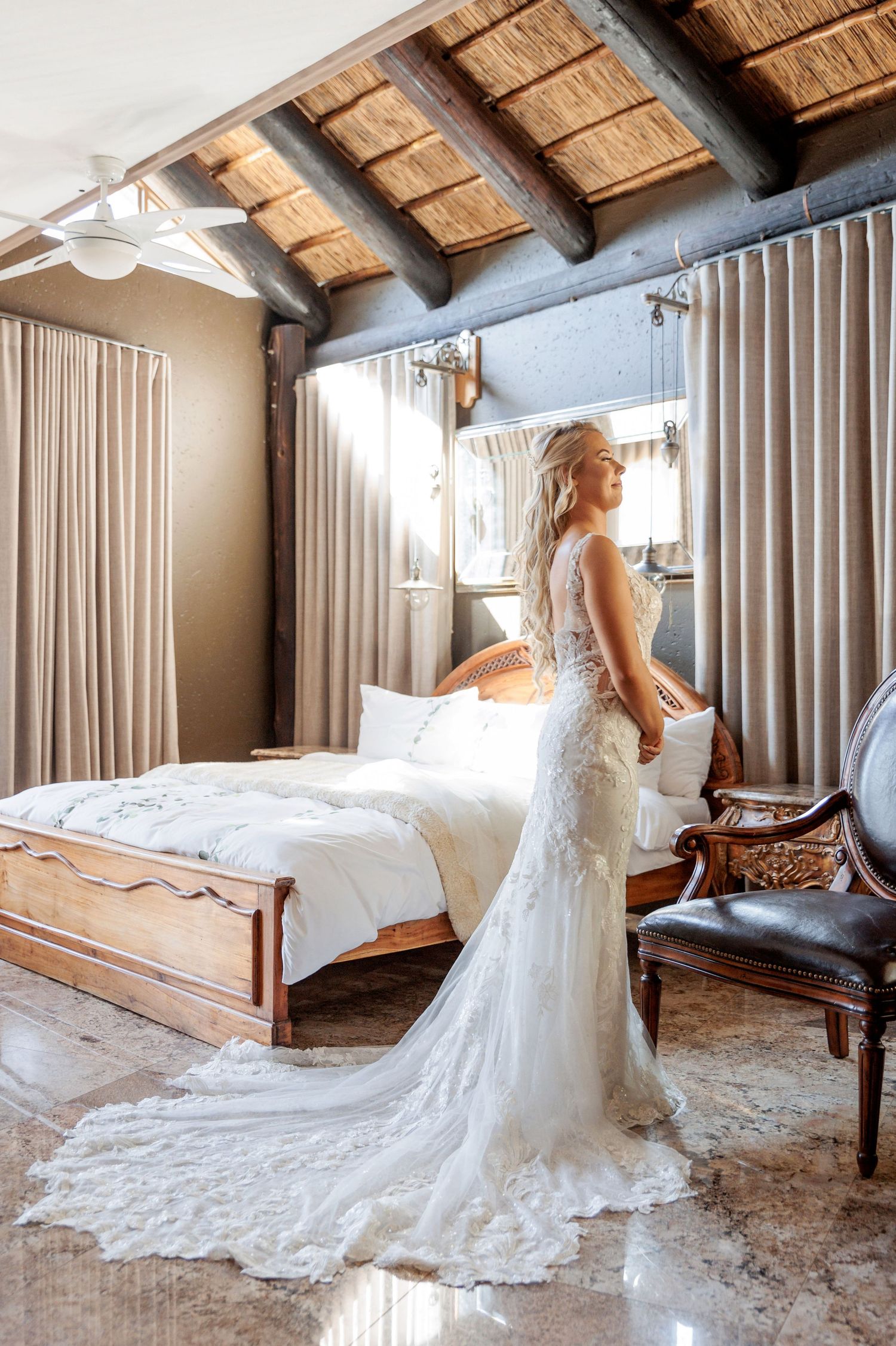 Wedding dress with long train displayed in rustic room with wooden beamed ceiling.