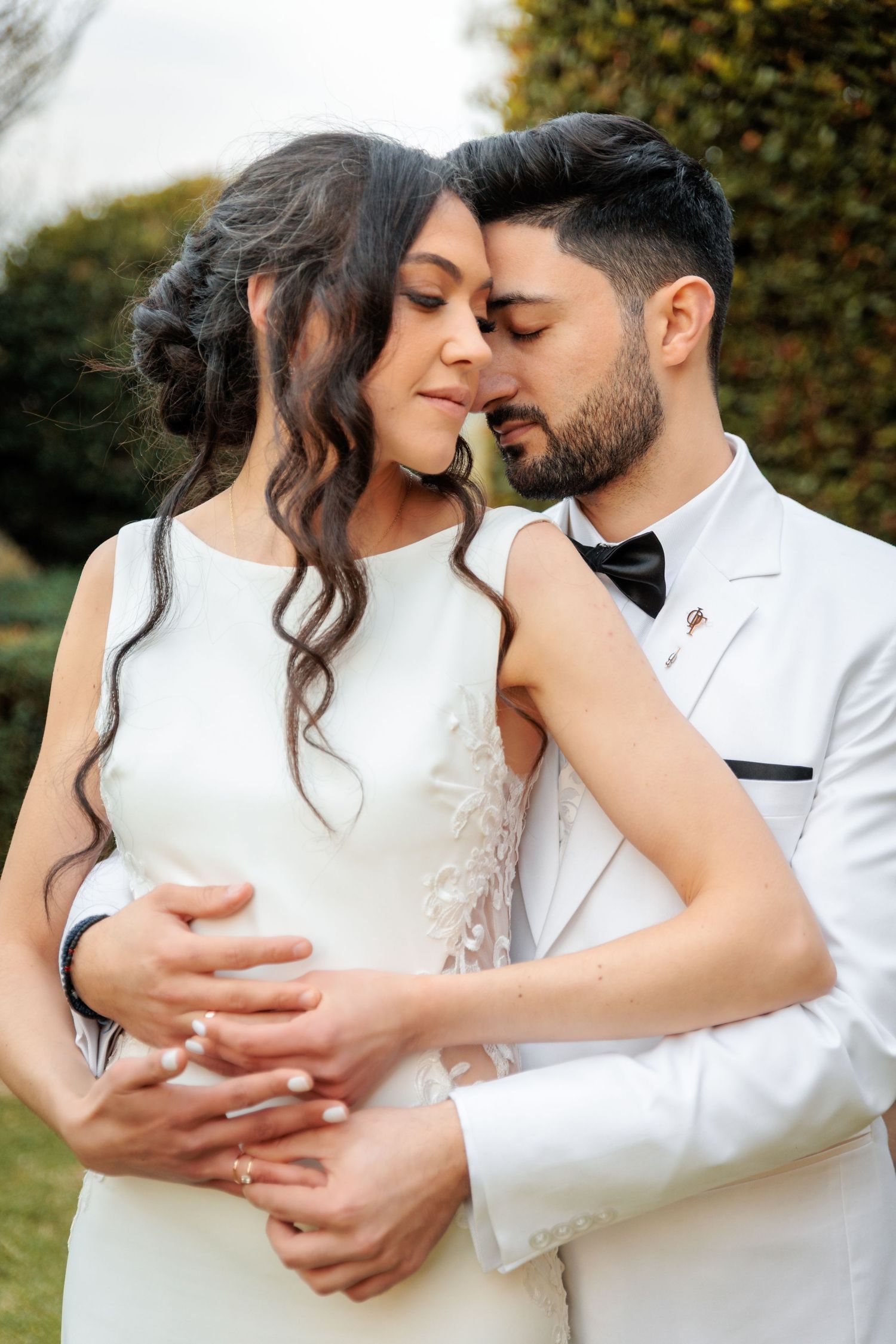 A couple in matching white outfits shares an intimate embrace outdoors.