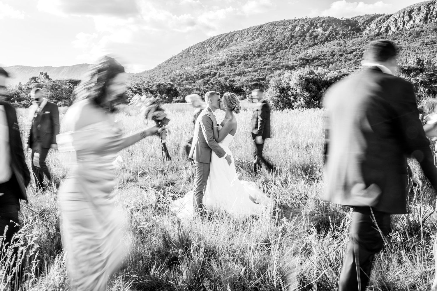 A blurred motion sequence of people walking along a mountain trail in black and white.
