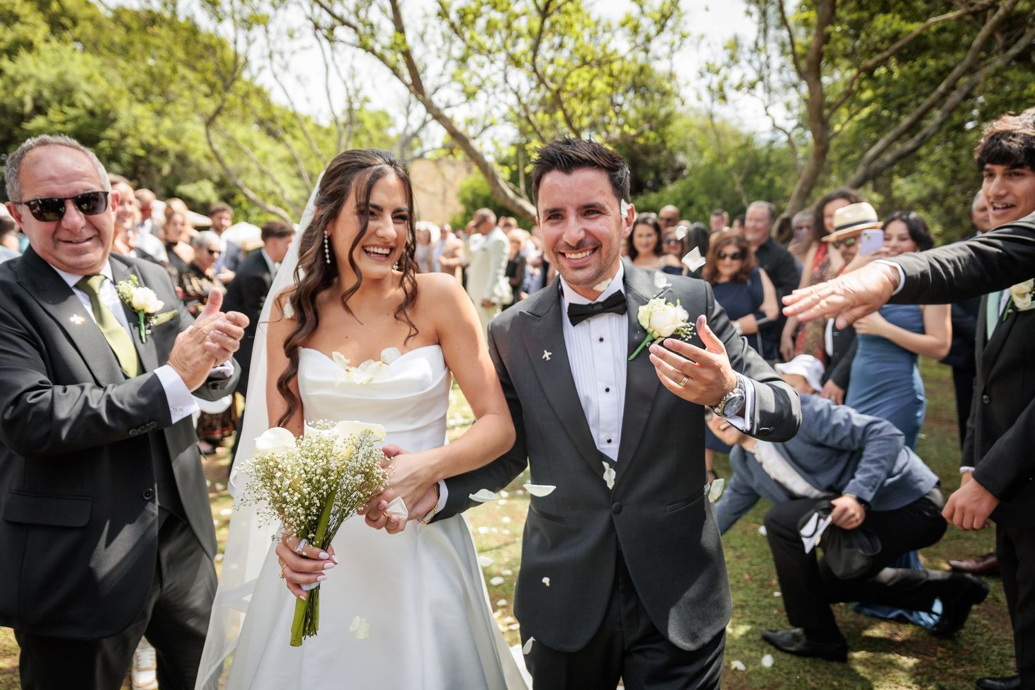 A wedding celebration with guests cheering and waving as the newlyweds walk down a garden path.