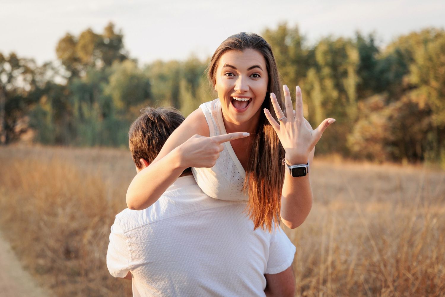 A joyful couple embraces and laughs together in a sunlit autumn field during a photoshoot.