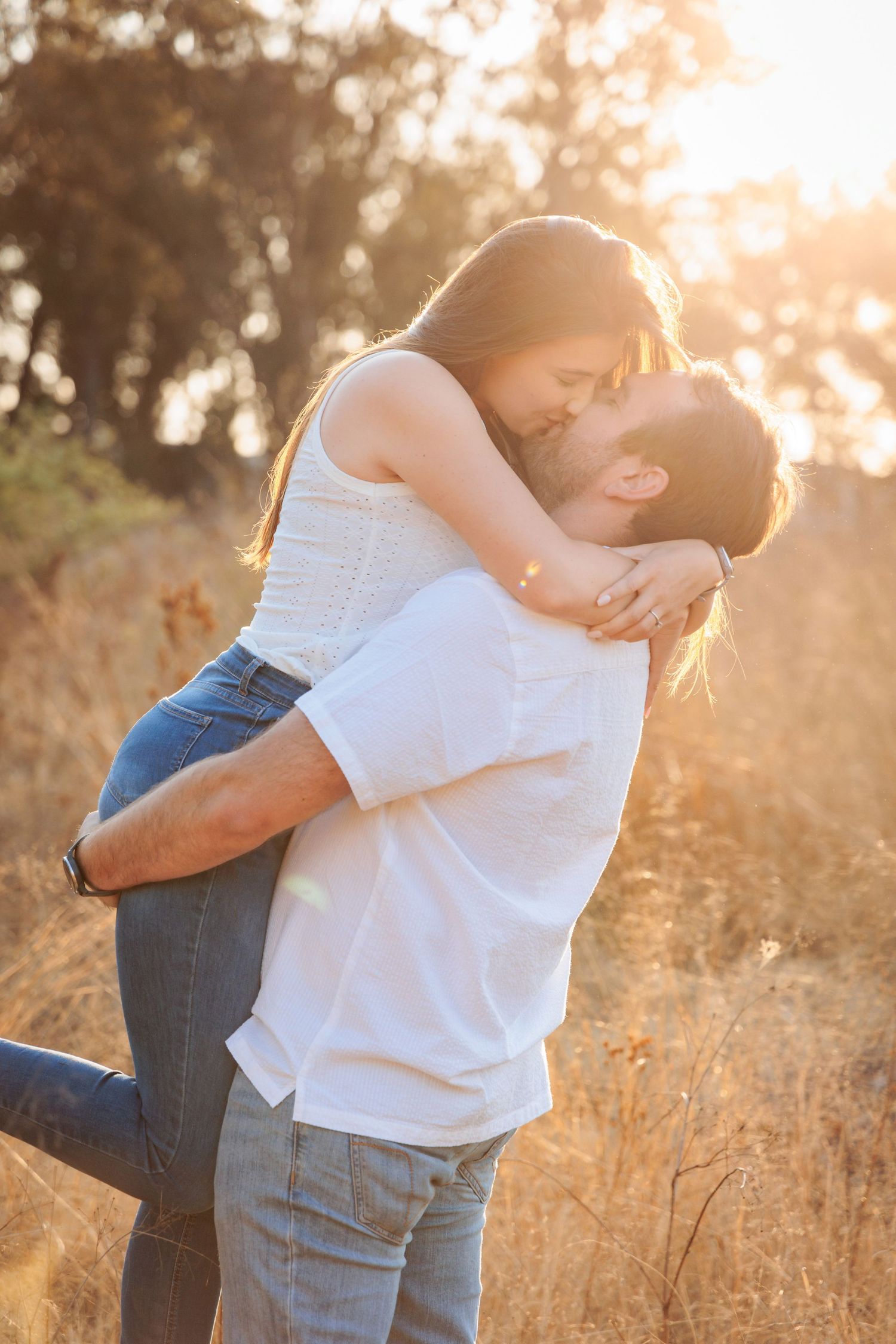 A couple embraces in a golden sunlit field during sunset, creating a romantic silhouette against the warm glowing backdrop.