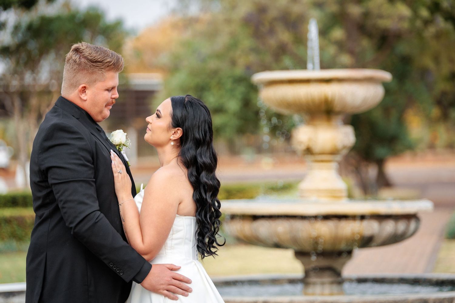 Intimate wedding photography session showing tender moments between newlyweds near a garden fountain.