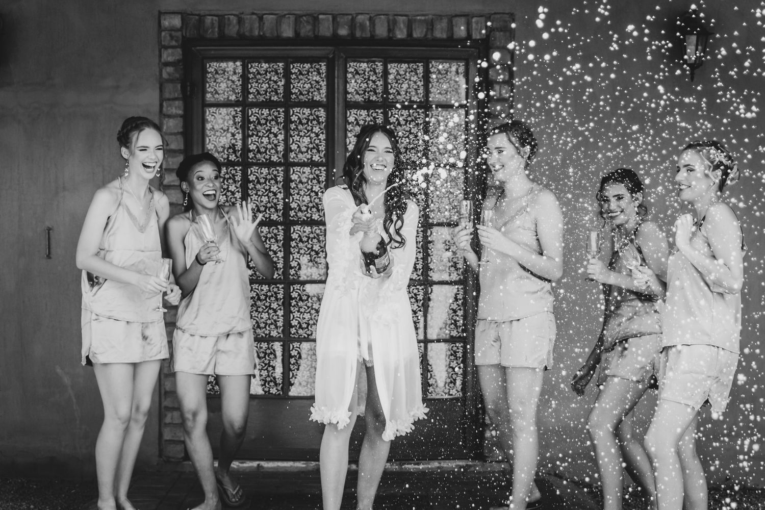 Wedding party in light colored outfits dancing under sparkling lights.