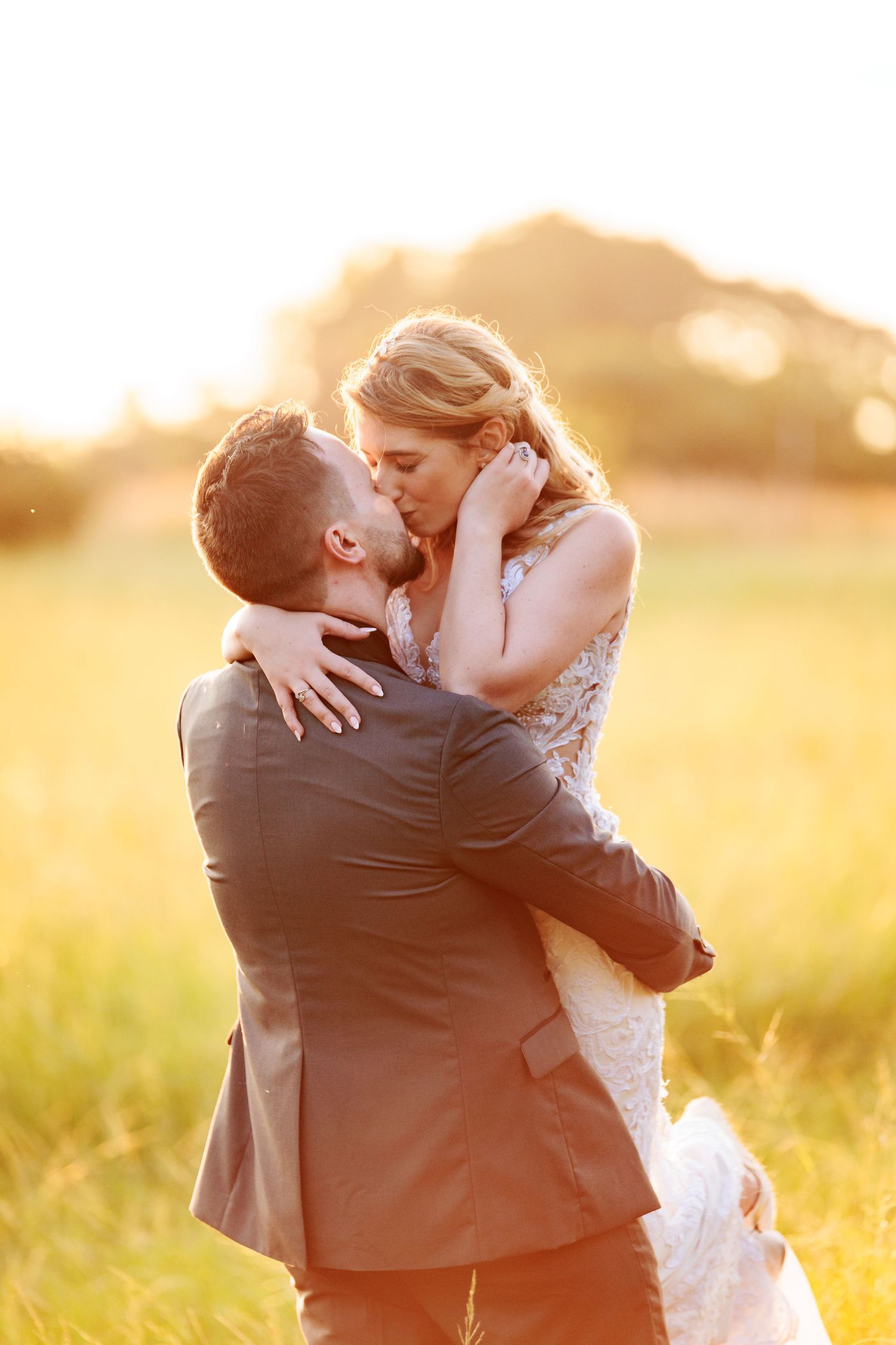 A romantic couple embraces in a golden sunlit field during sunset creating a dreamy wedding portrait series.