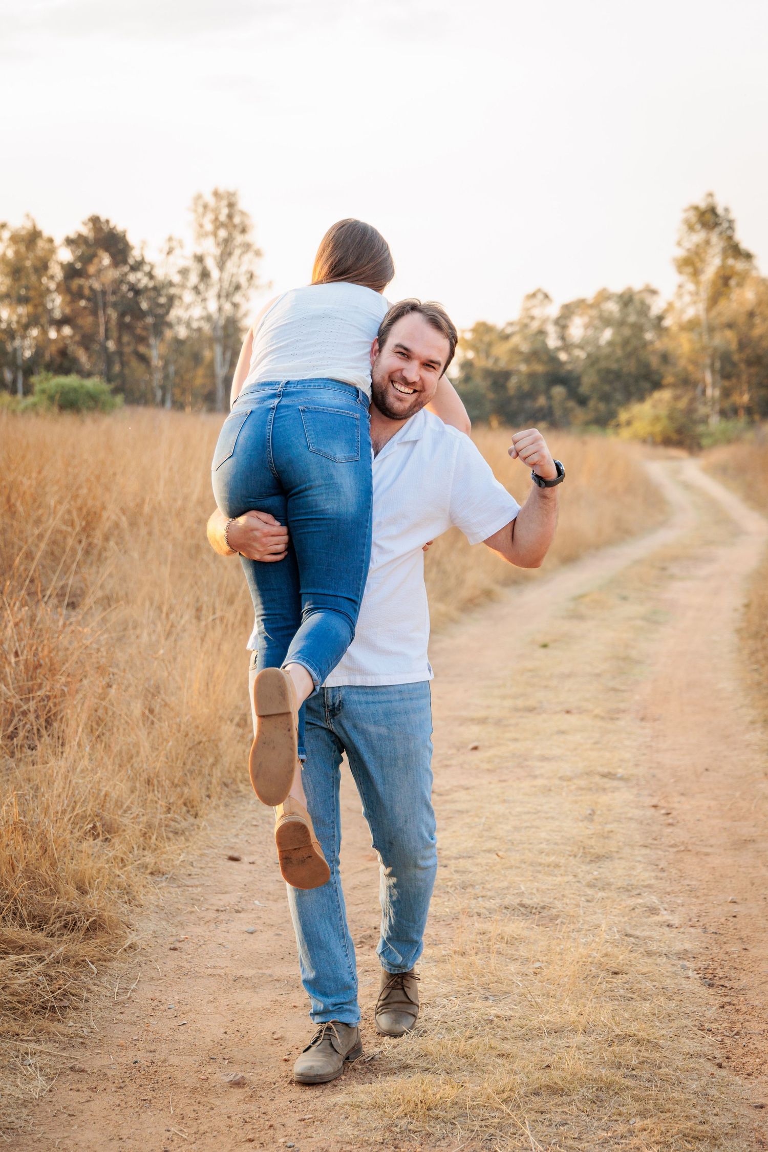 A joyful moment shared between two people walking on a dirt path through golden grass at sunset.