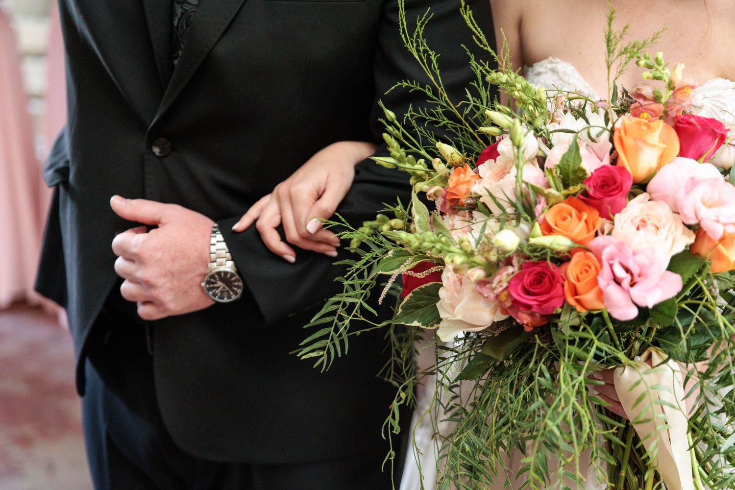 Wedding party members hold vibrant floral bouquets with coral and pink roses against formal black attire.
