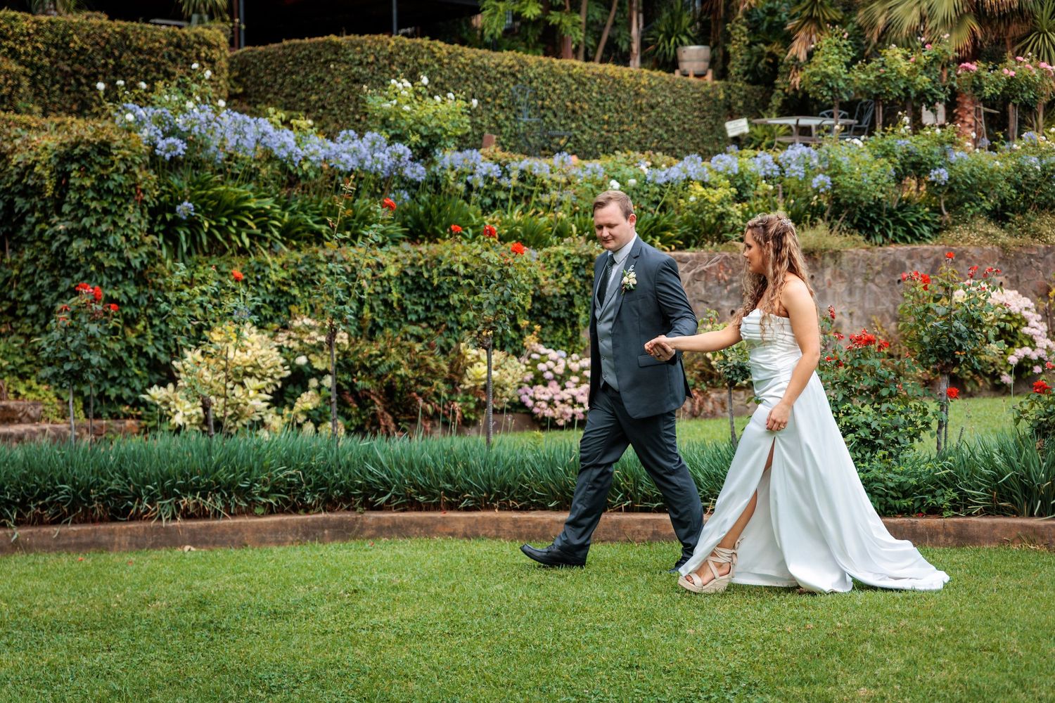 Wedding couple running playfully through a lush garden landscape.