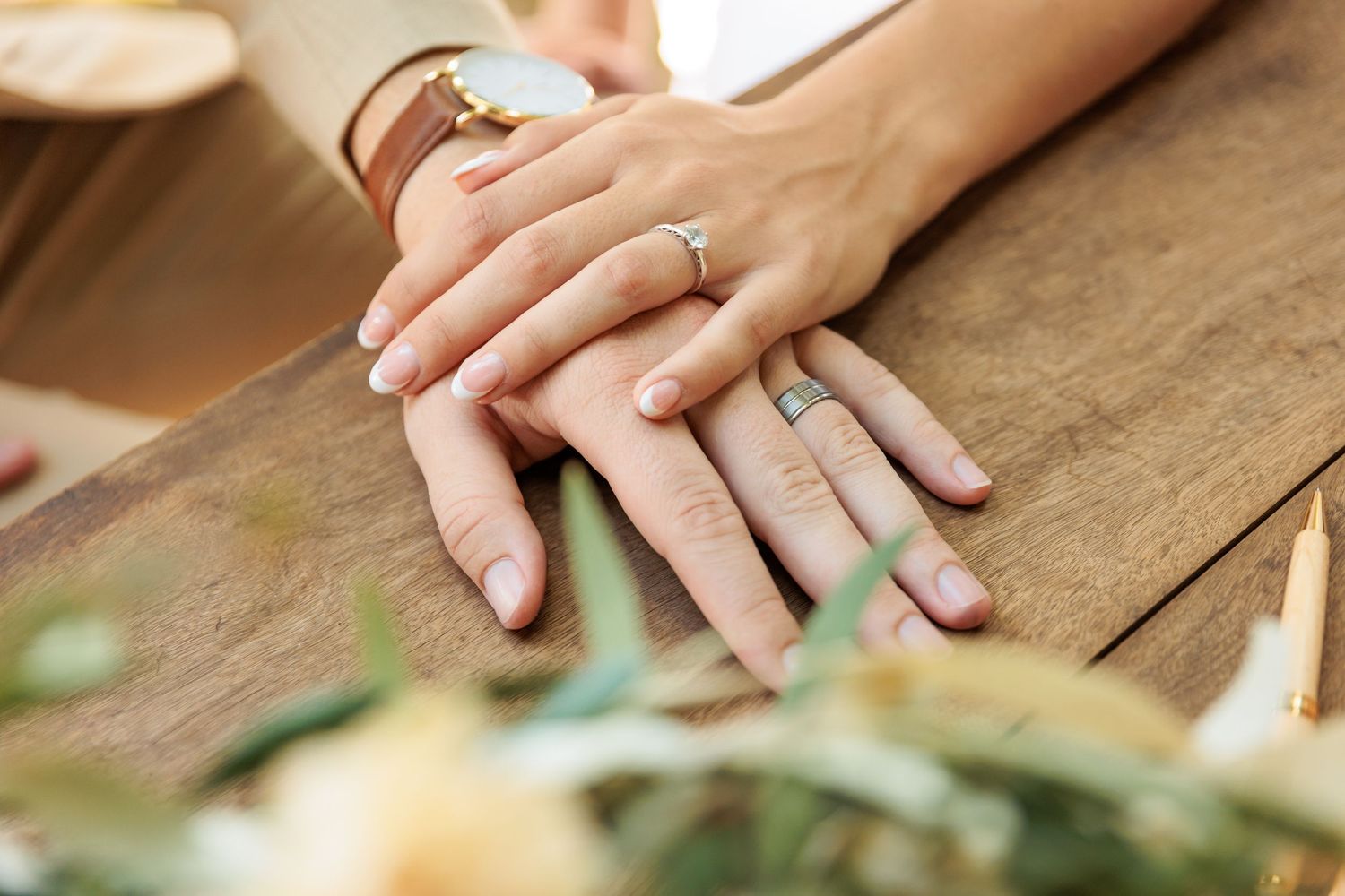 Close-up of newlywed hands with wedding rings resting on wooden surface.