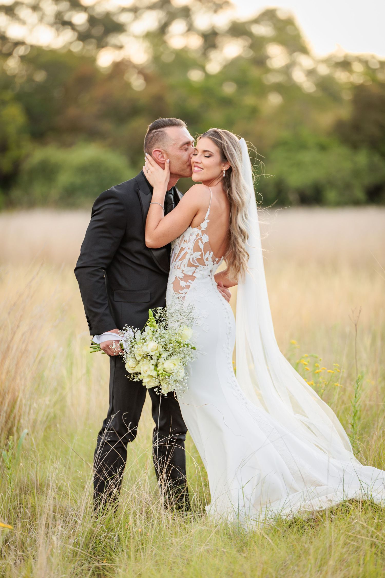 Romantic wedding couple shares intimate moments in a golden sunlit meadow with flowing white dress and bouquet.