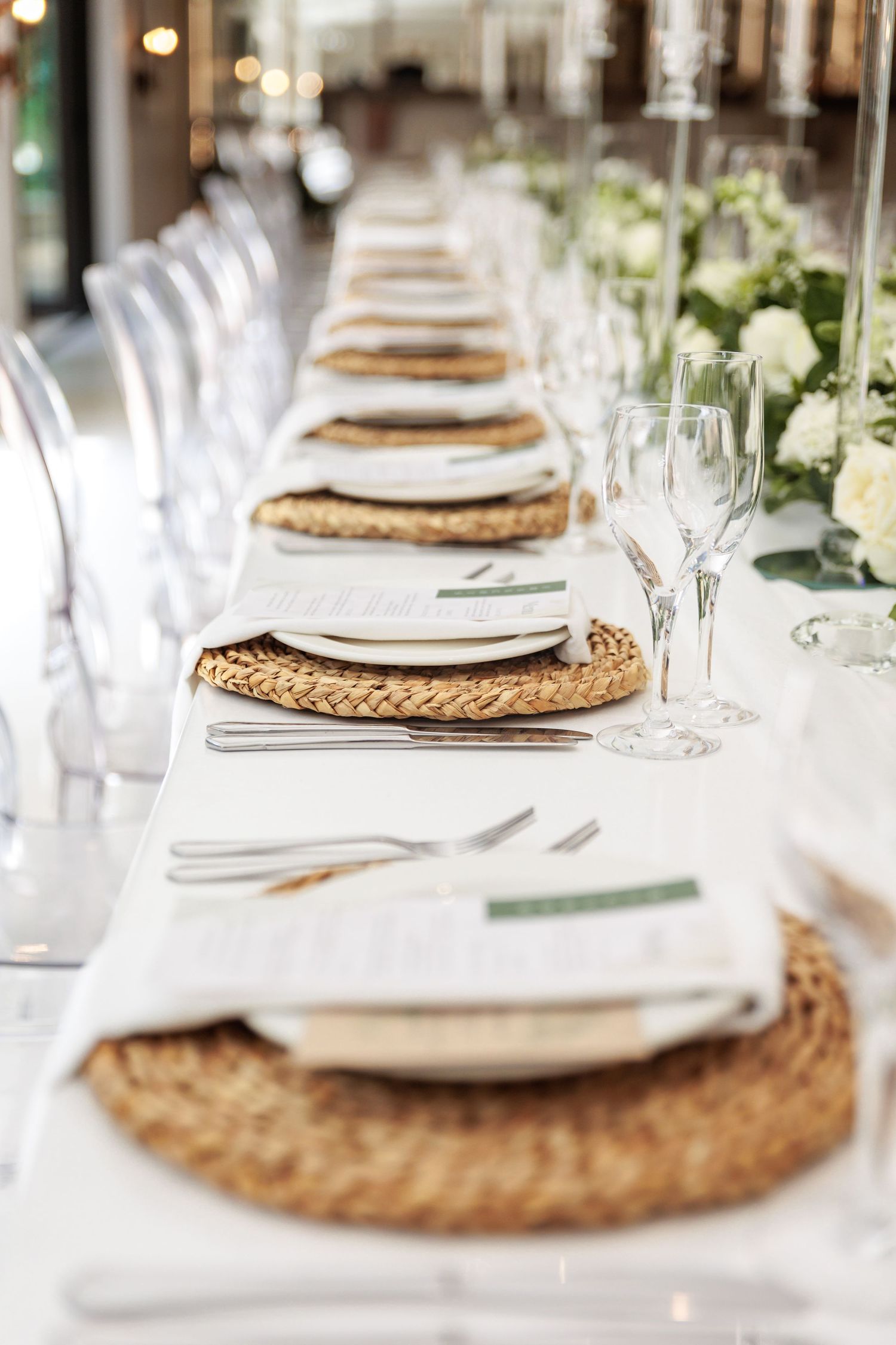 Elegant table settings with woven rattan chargers, white plates, and eucalyptus greenery at a formal dining event.