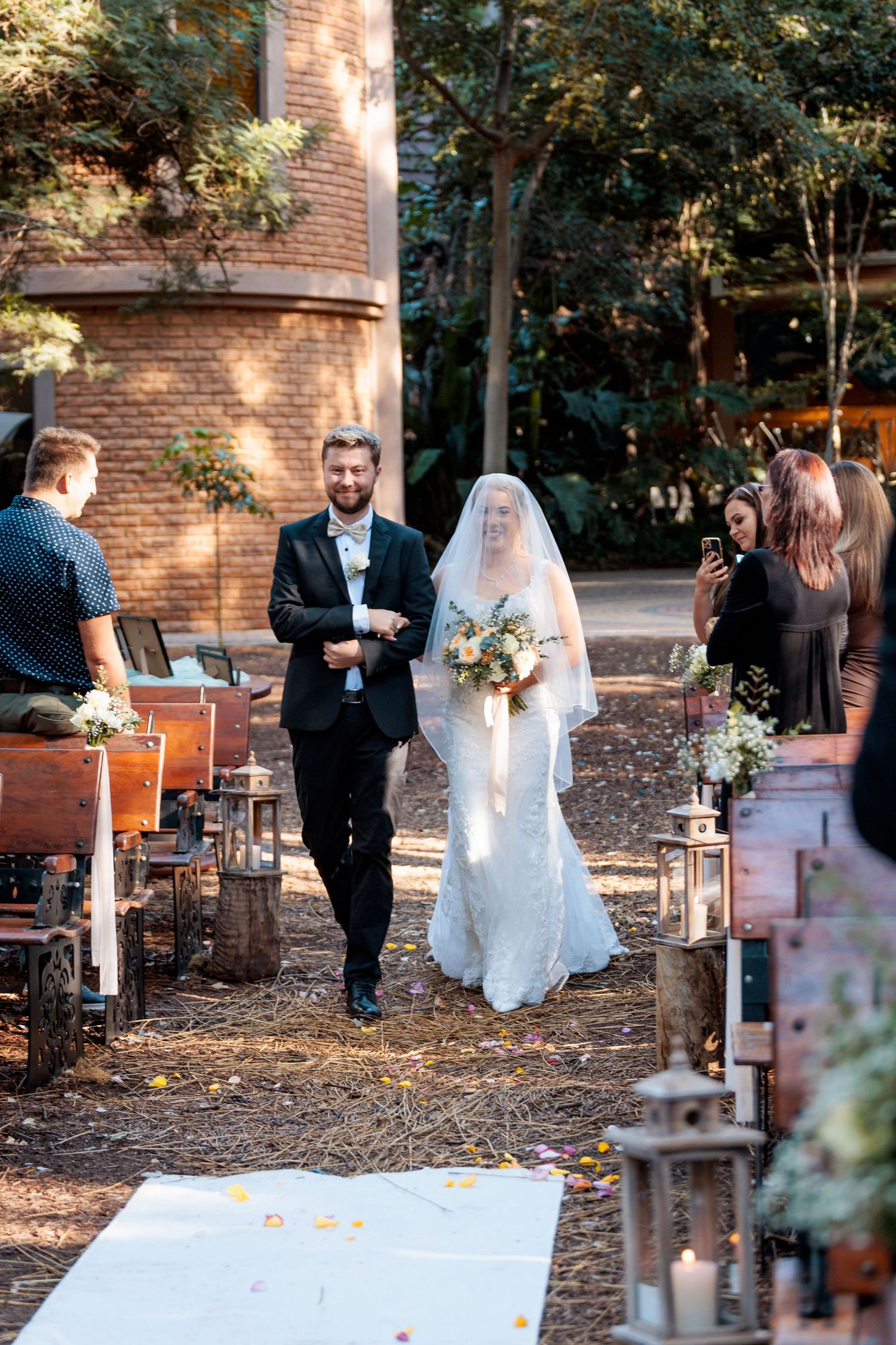 Wedding ceremony setup in a rustic outdoor setting with wooden chairs and white aisle runner at sunset.