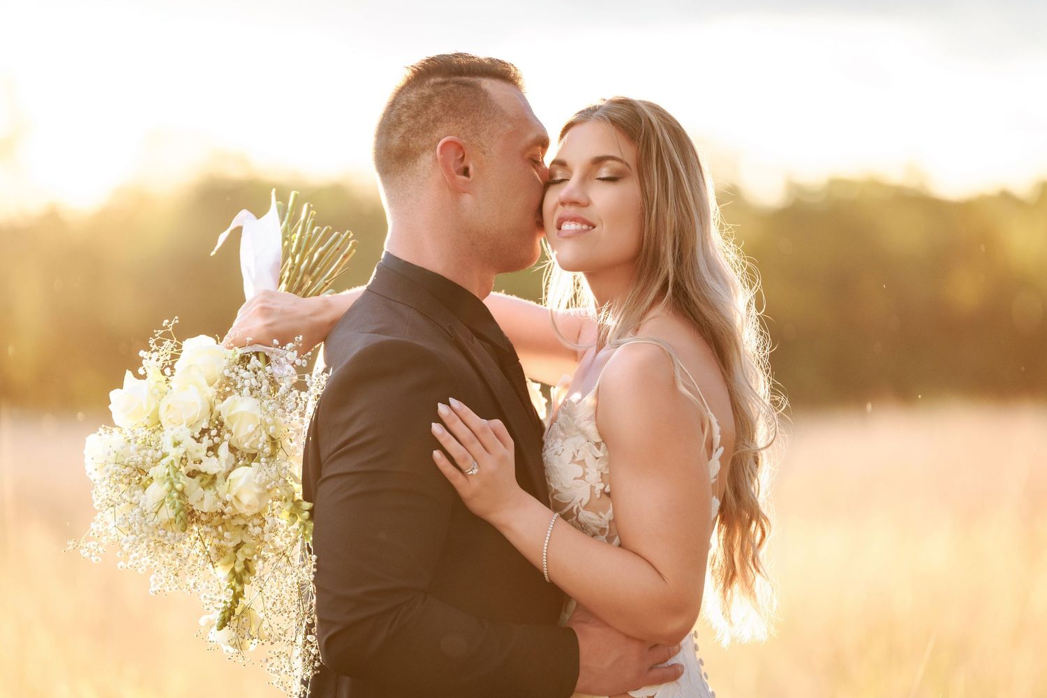 A couple shares an intimate moment during their wedding photoshoot at golden hour in a sunlit field.