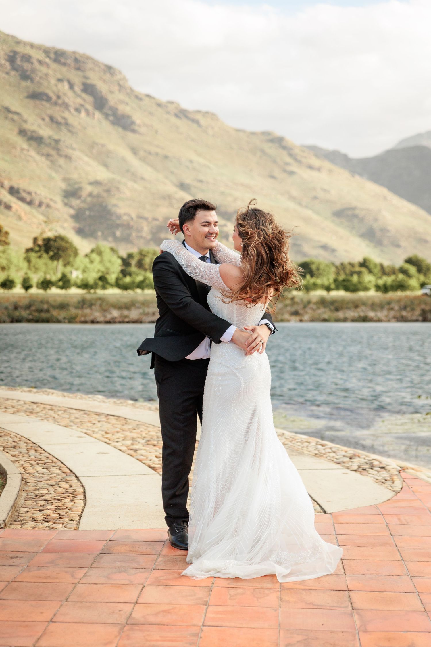 A couple shares a romantic dance pose on a terrace overlooking a scenic mountain lake on their wedding day.