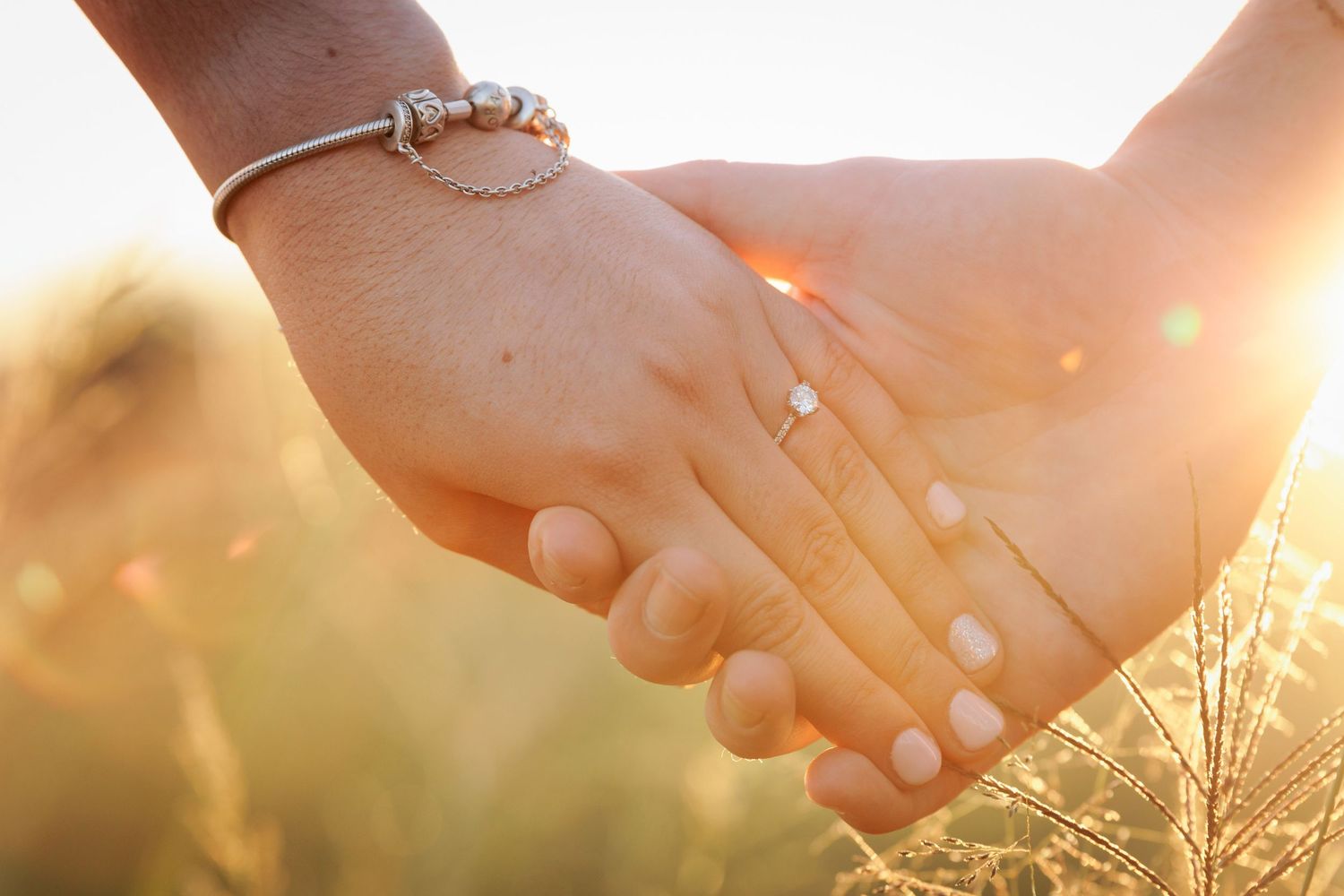 Two people hold hands in a romantic sunset moment with golden light shining through their fingers.