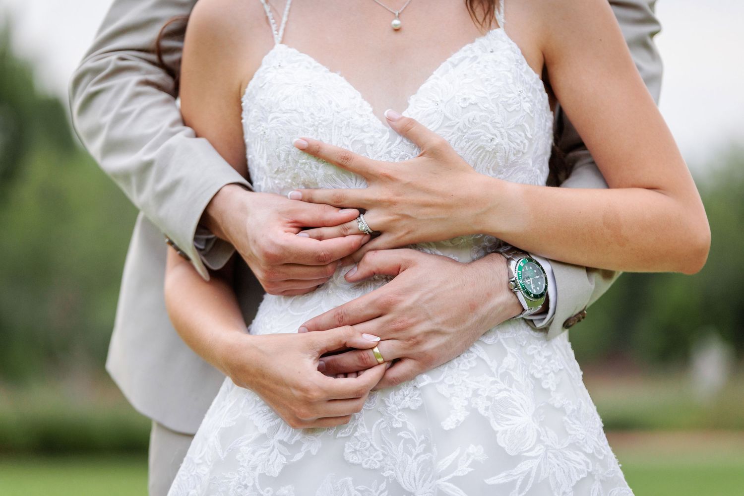 Close-up details of a white lace wedding dress and loving embrace.