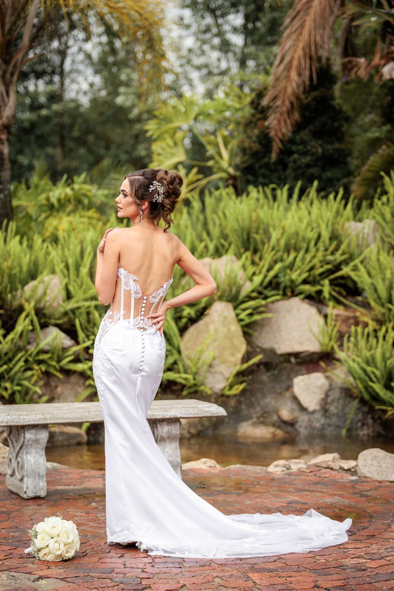 Elegant white wedding dress with corset back and long train photographed in a lush tropical garden setting.