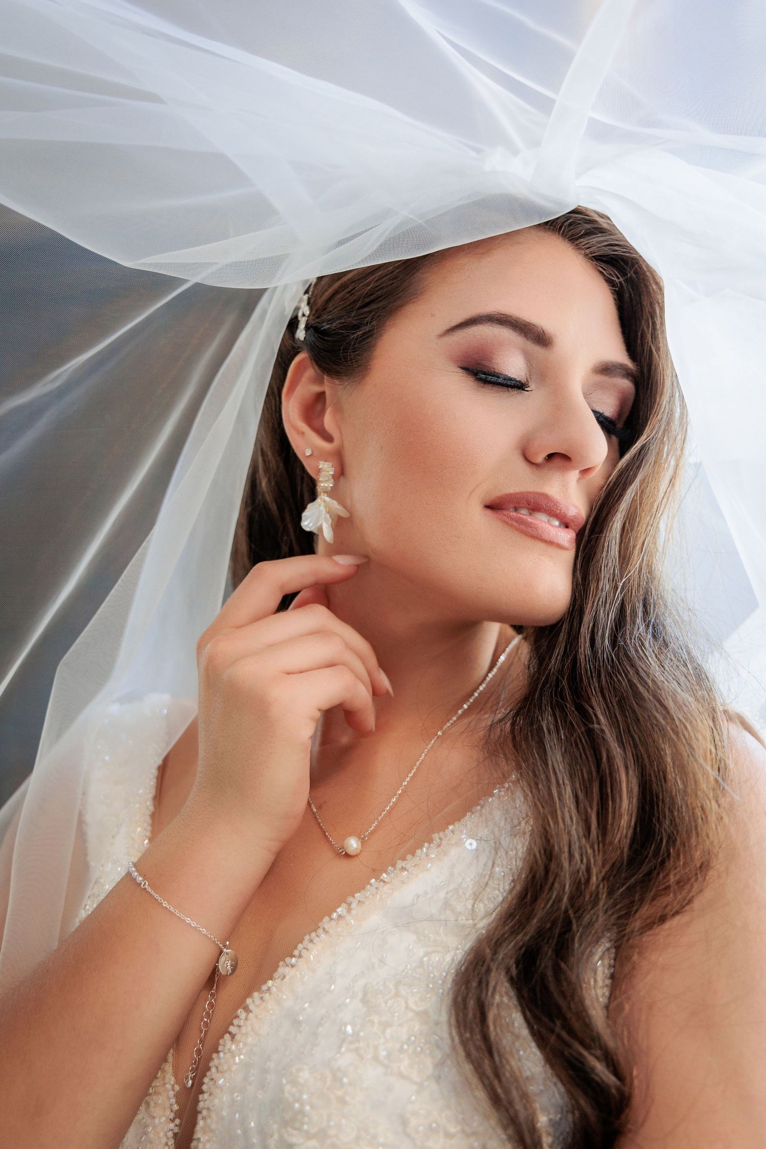 Artistic bridal portrait with flowing veil and delicate jewelry details.