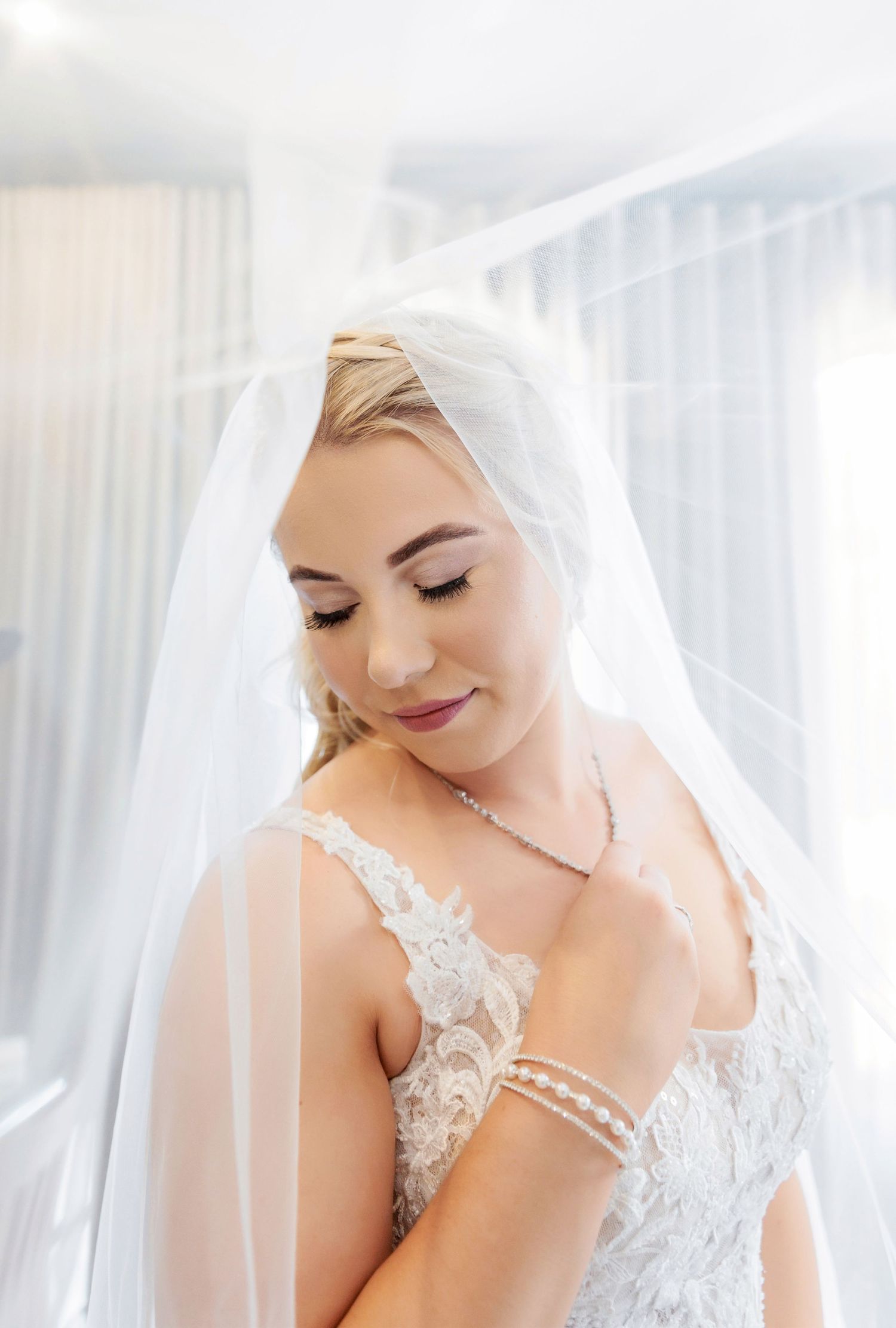 Delicate lace wedding gown details with veil in soft window light.