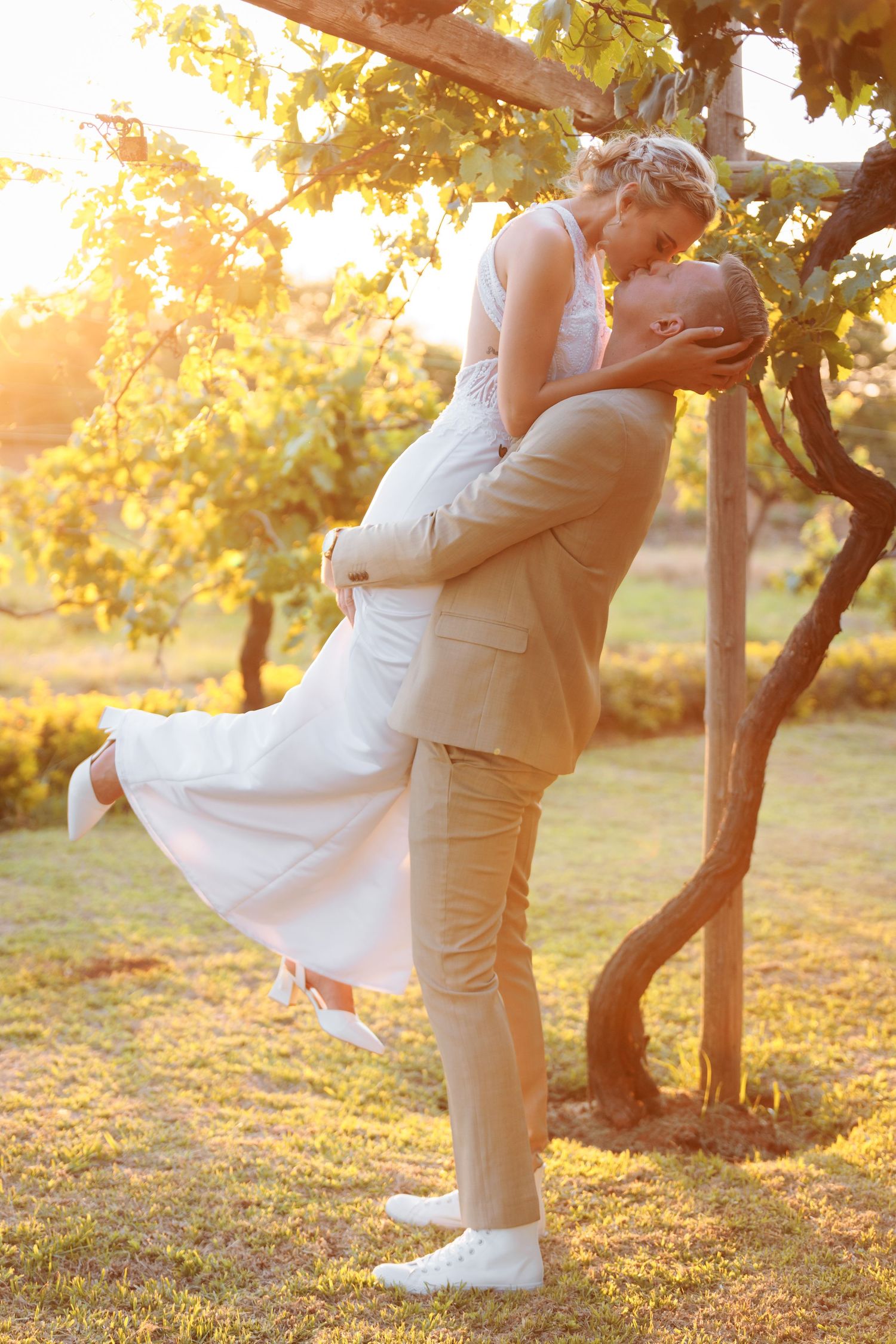 A romantic sunset lift pose between newlyweds in an orchard setting.