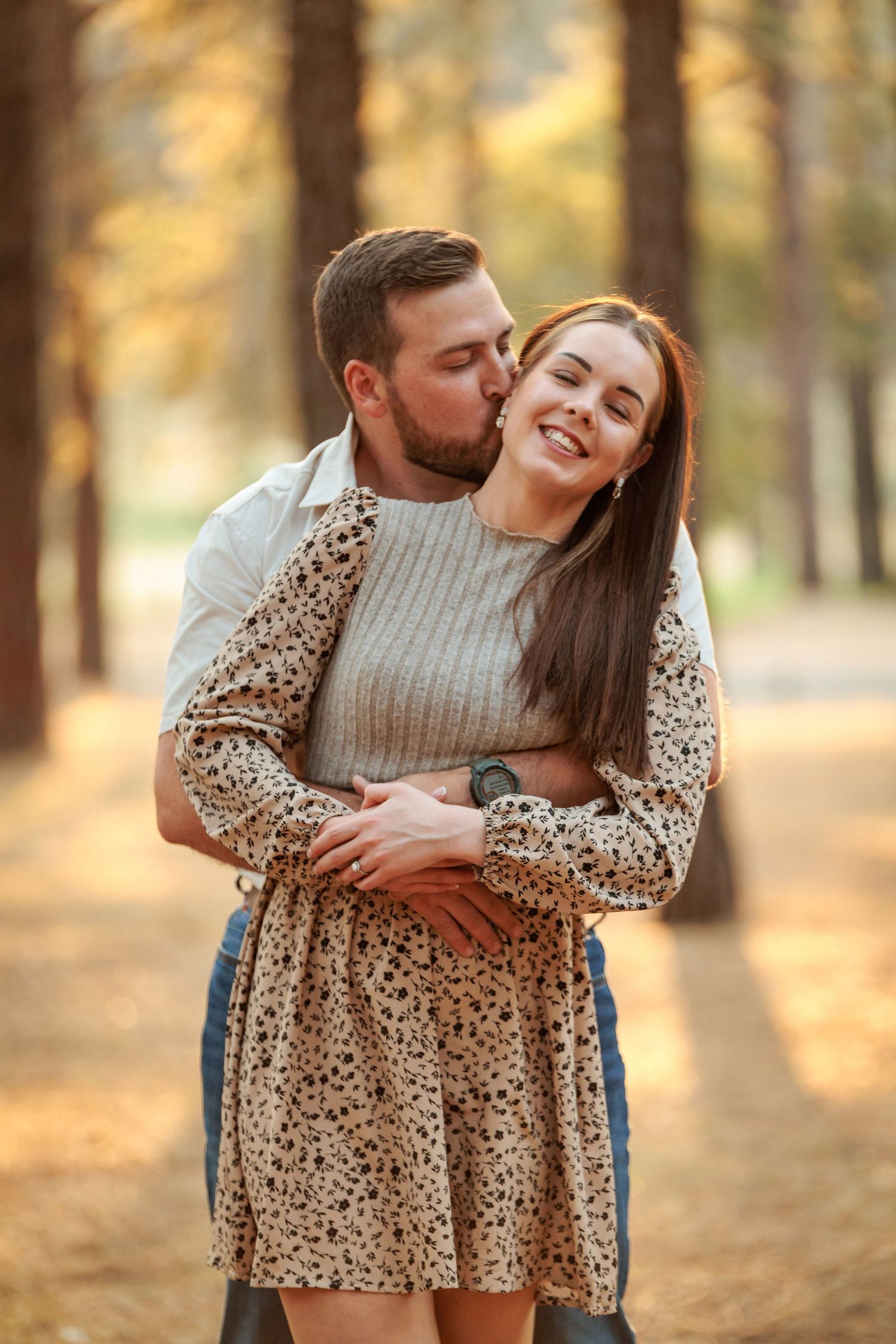 Romantic autumn engagement photos showing a couple embracing in a sunlit forest with warm golden tones.