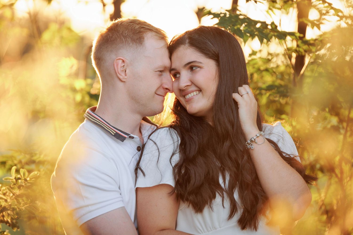A couple embraces in a romantic golden sunset with sunlight filtering through trees in the background.