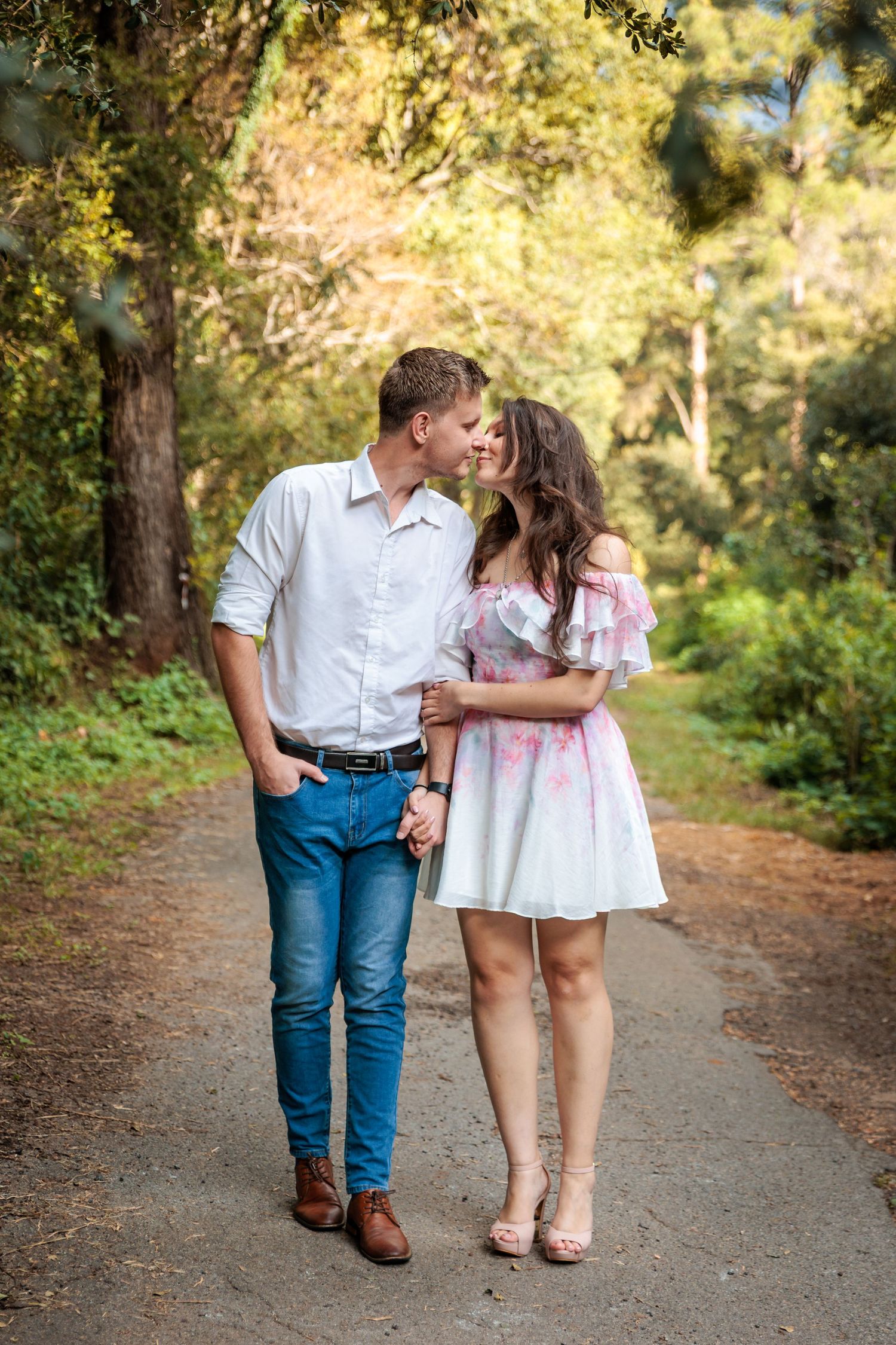 A romantic couple shares a tender moment while walking along a tree-lined path on a sunny autumn day.