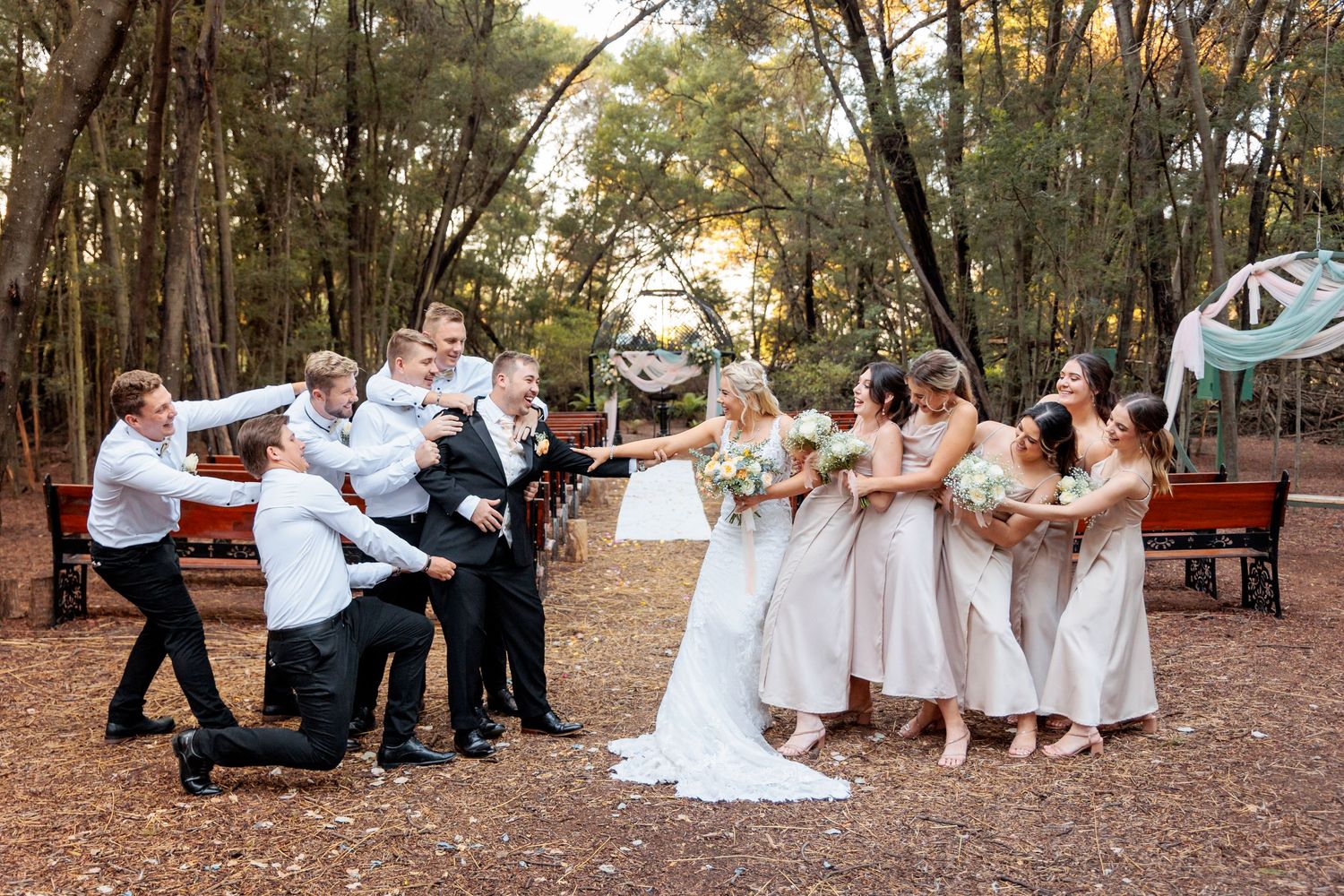 Playful wedding party posing in a line on fallen autumn leaves in a park setting.
