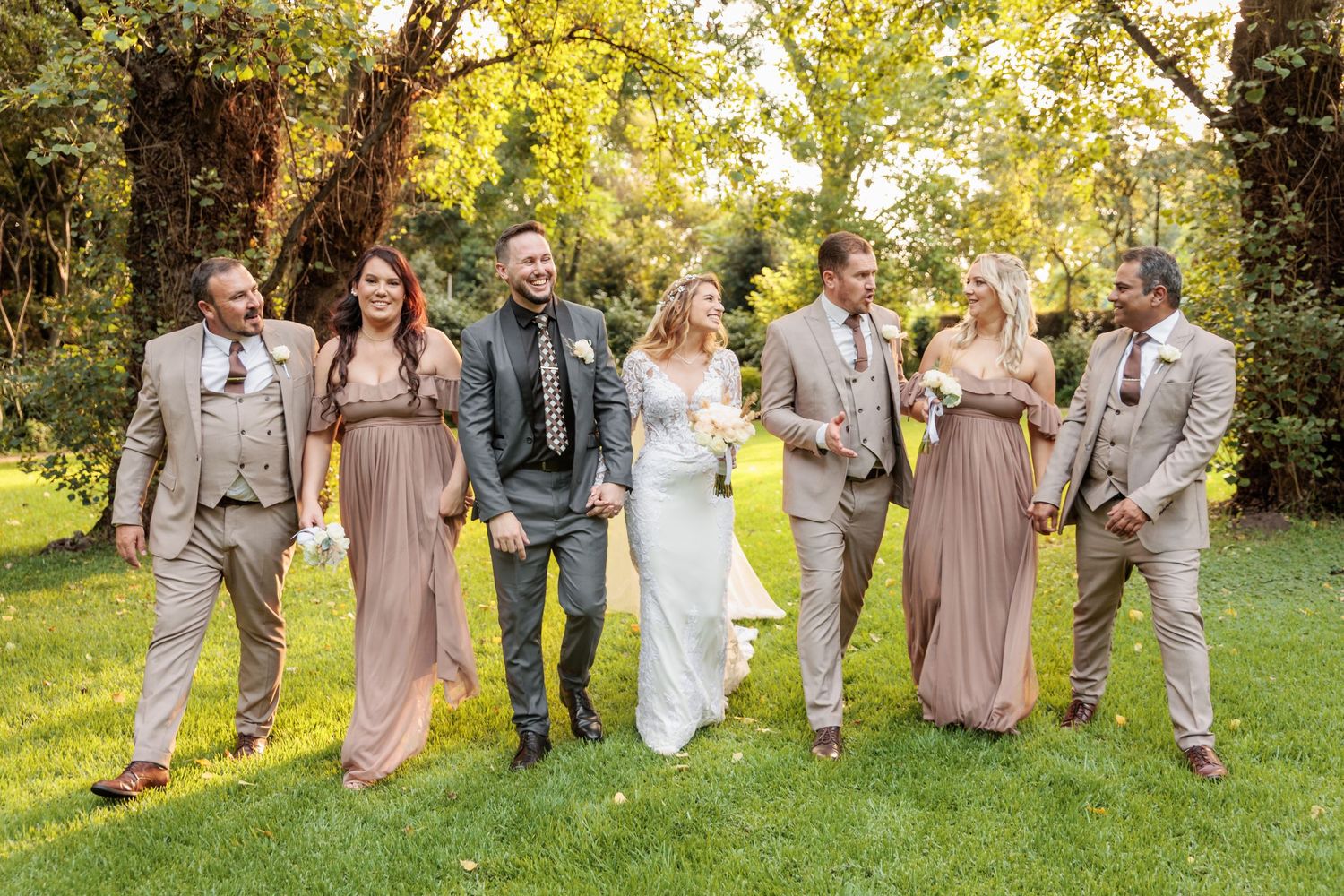 Wedding party walks and laughs together on grassy lawn during golden hour sunset photography session.