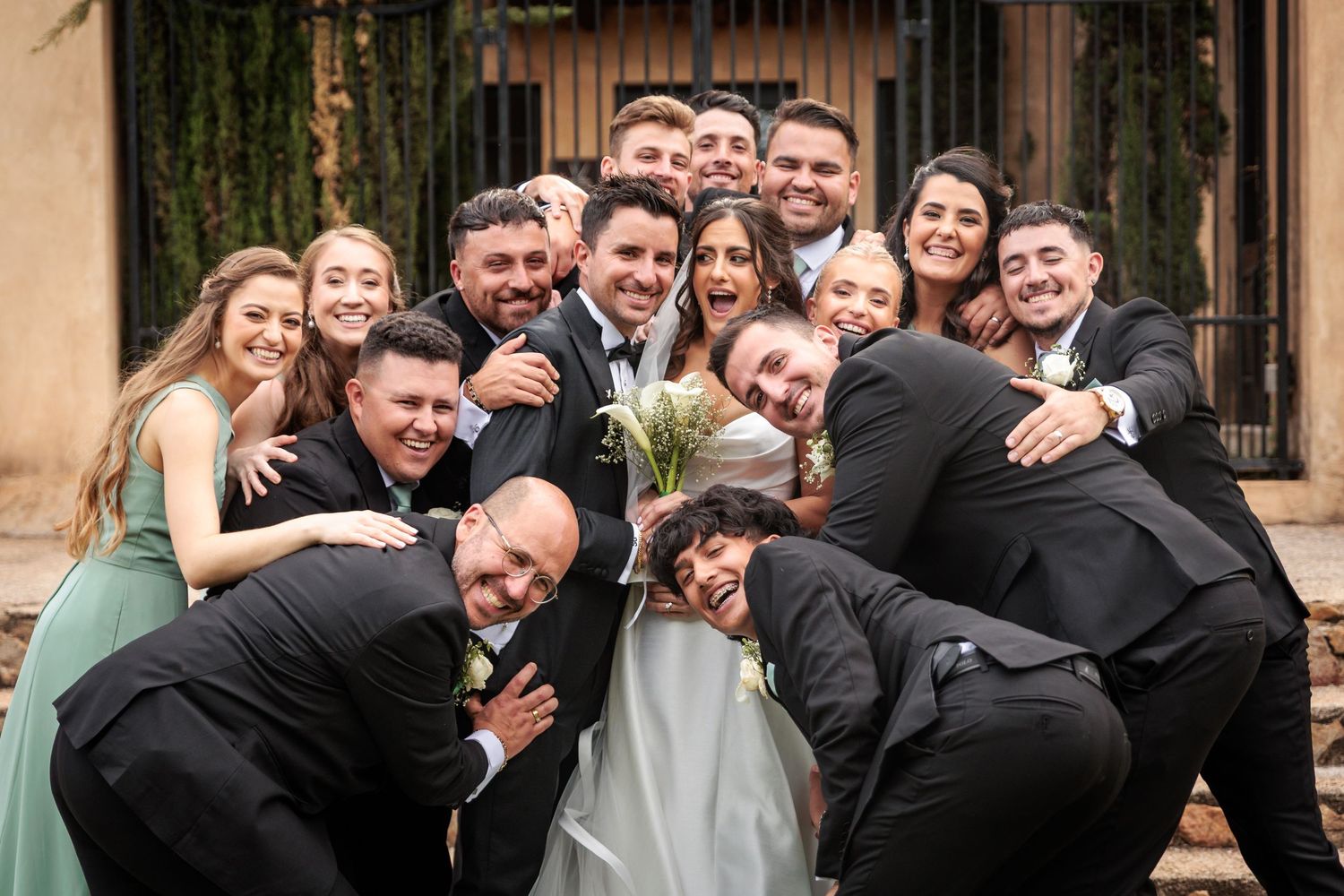 A joyful group photo at a wedding with people laughing and embracing in formal attire.