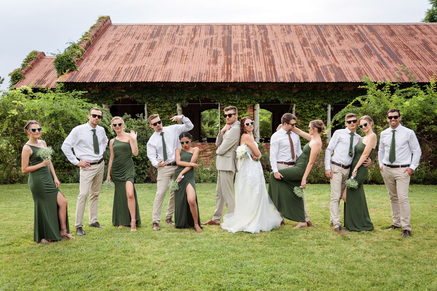 Wedding party poses creatively on grass in alternating positions wearing sage green and khaki attire.