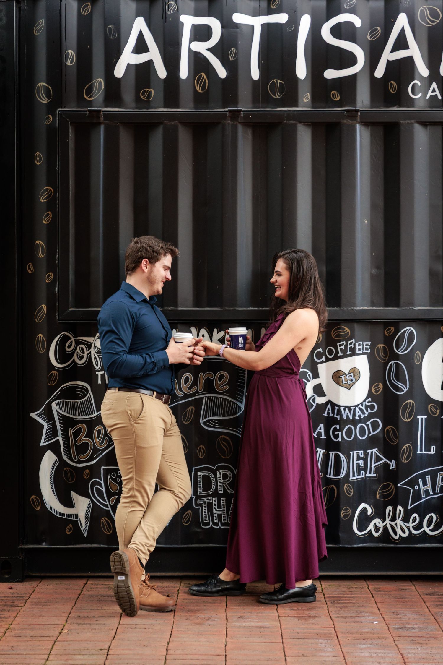 A couple shares a romantic moment in front of a chalkboard wall at an artisan coffee shop.