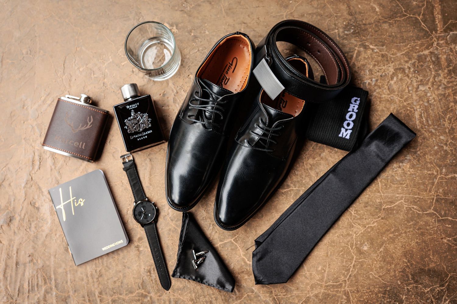 Wedding day accessories including dress shoes, socks, and personal items arranged on wooden surface.