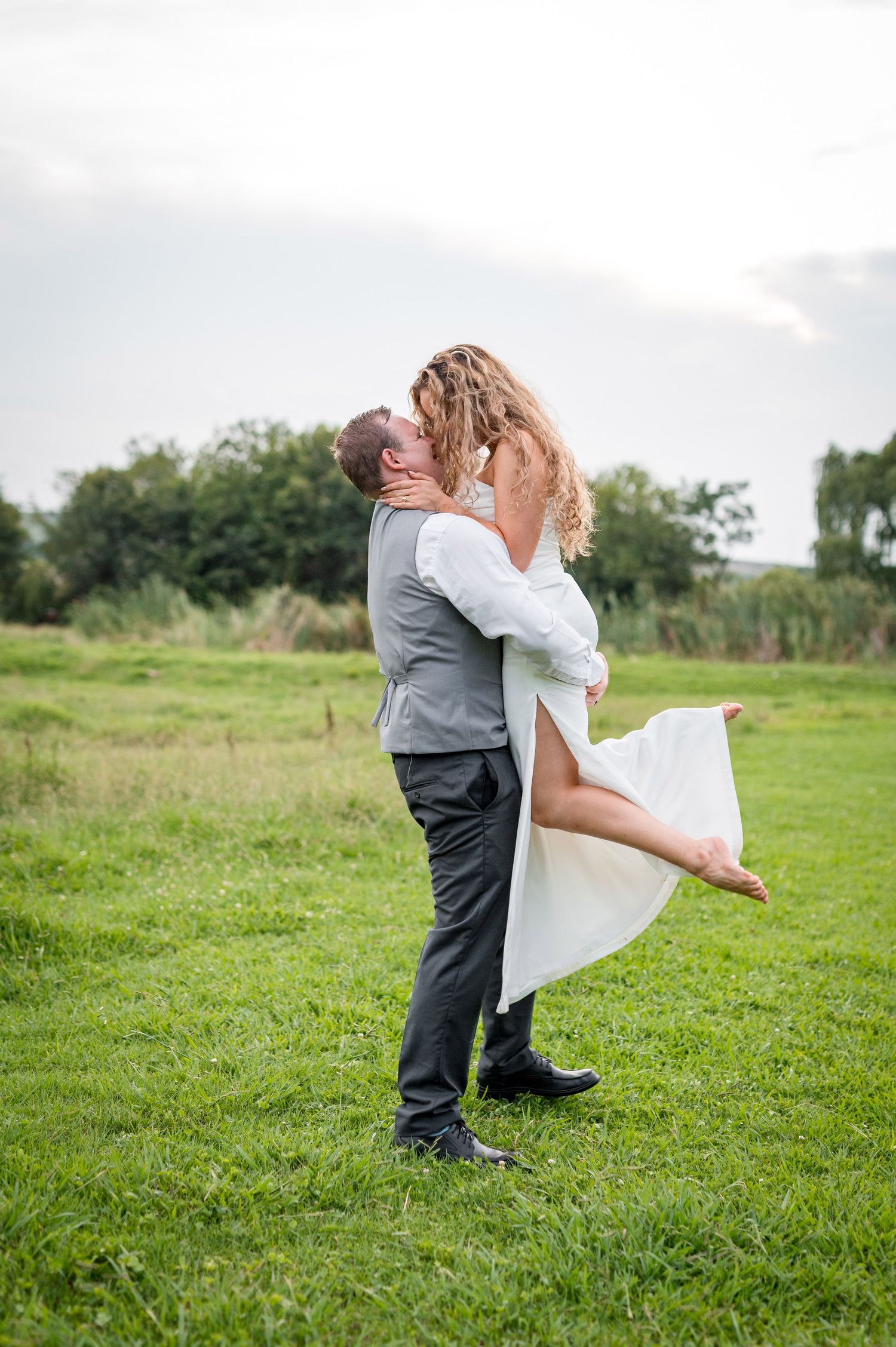A romantic embrace on a grassy field with trees in the background.