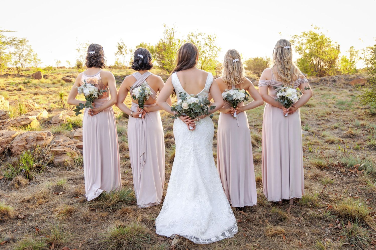 Bridesmaids in blush pink dresses pose together outdoors at sunset.