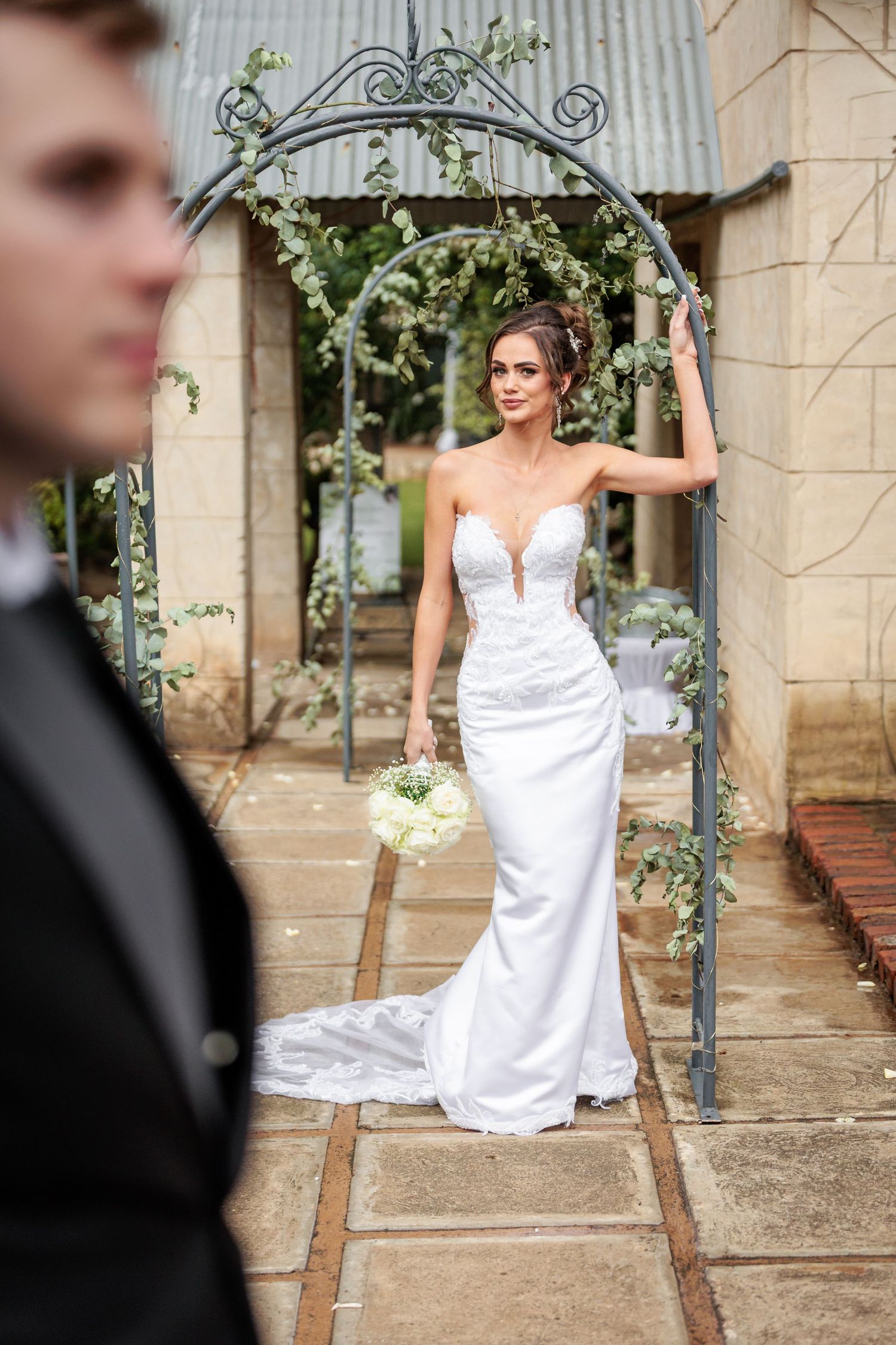 A wedding photoshoot series featuring a bride in a white gown posing elegantly against stone columns and greenery.