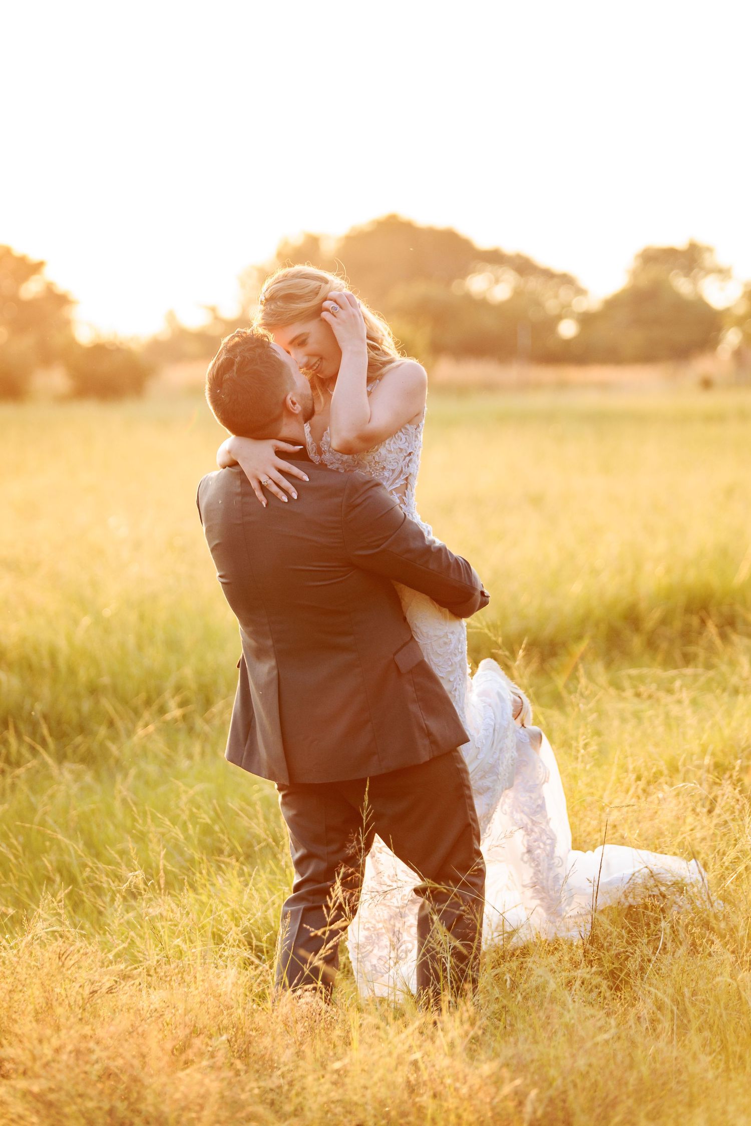 A romantic couple embraces in a golden sunlit field during sunset creating a dreamy silhouette effect.