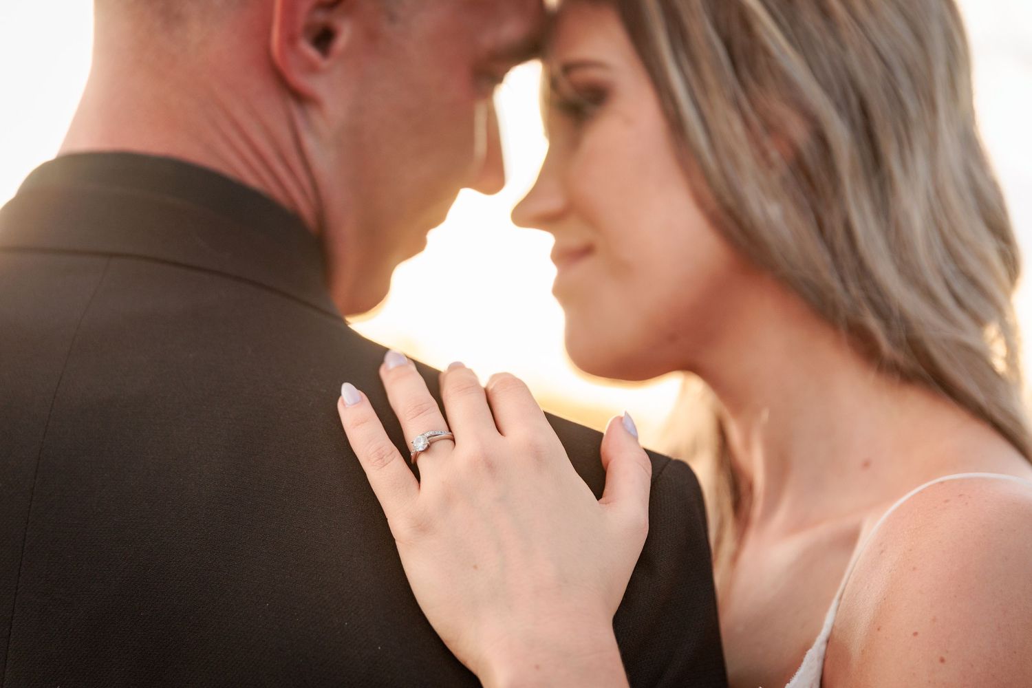 Romantic couple in formal attire dancing together at sunset during their wedding celebration.