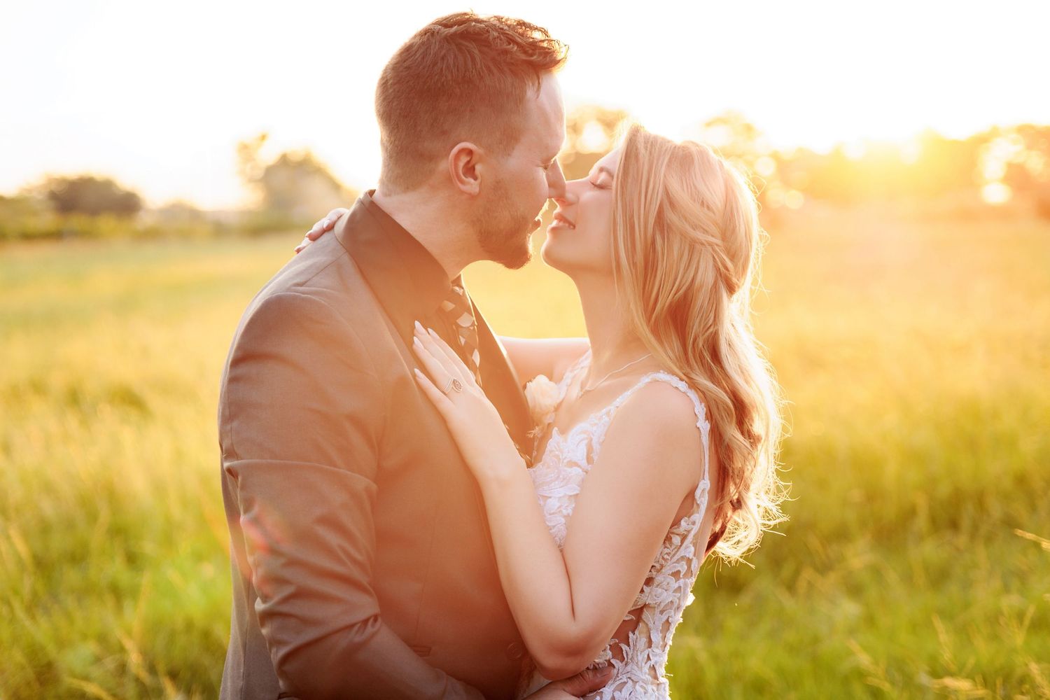 A romantic couple embraces in a golden sunlit field during sunset, creating a dreamy backlit silhouette.