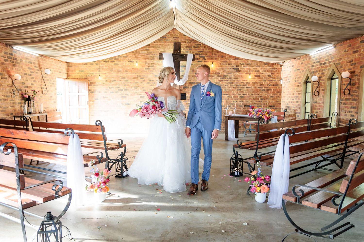 Interior view of a rustic barn wedding venue with draped fabric ceiling and exposed brick walls.