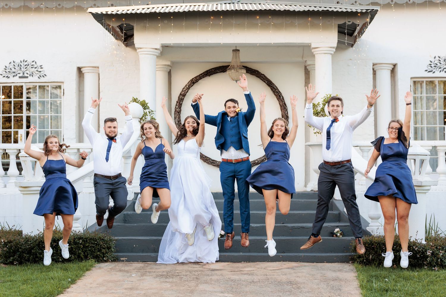 Wedding party jumps for joy on the steps of a classic white building.