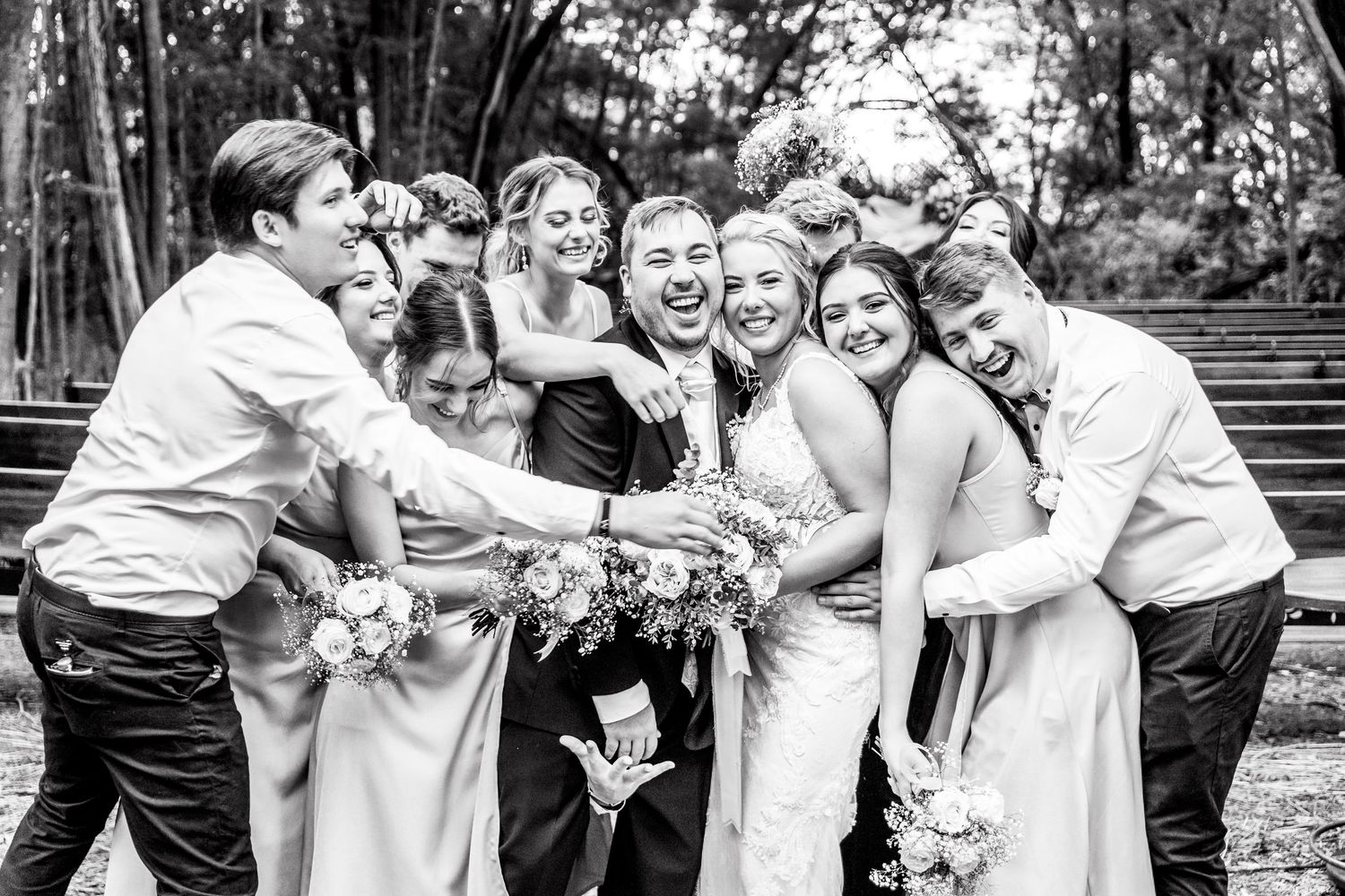 Black and white photo of wedding party laughing and embracing in casual group poses.