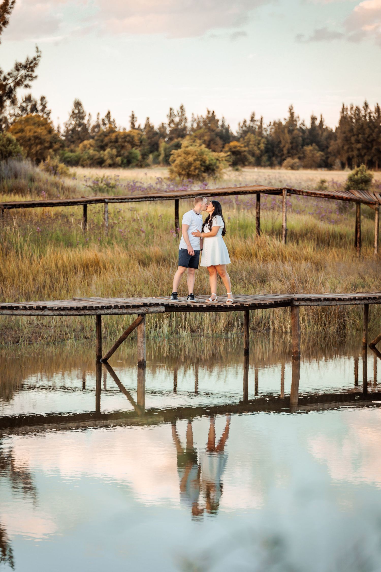 A wooden boardwalk stretches across a tranquil marsh with reflections in the still water at sunset.