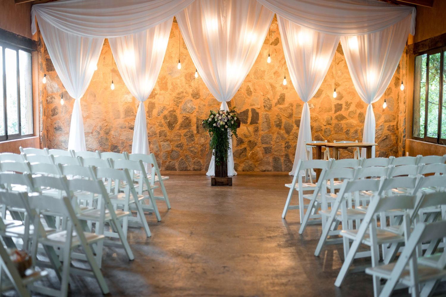 Elegant indoor wedding ceremony space with white draping and rows of chairs.