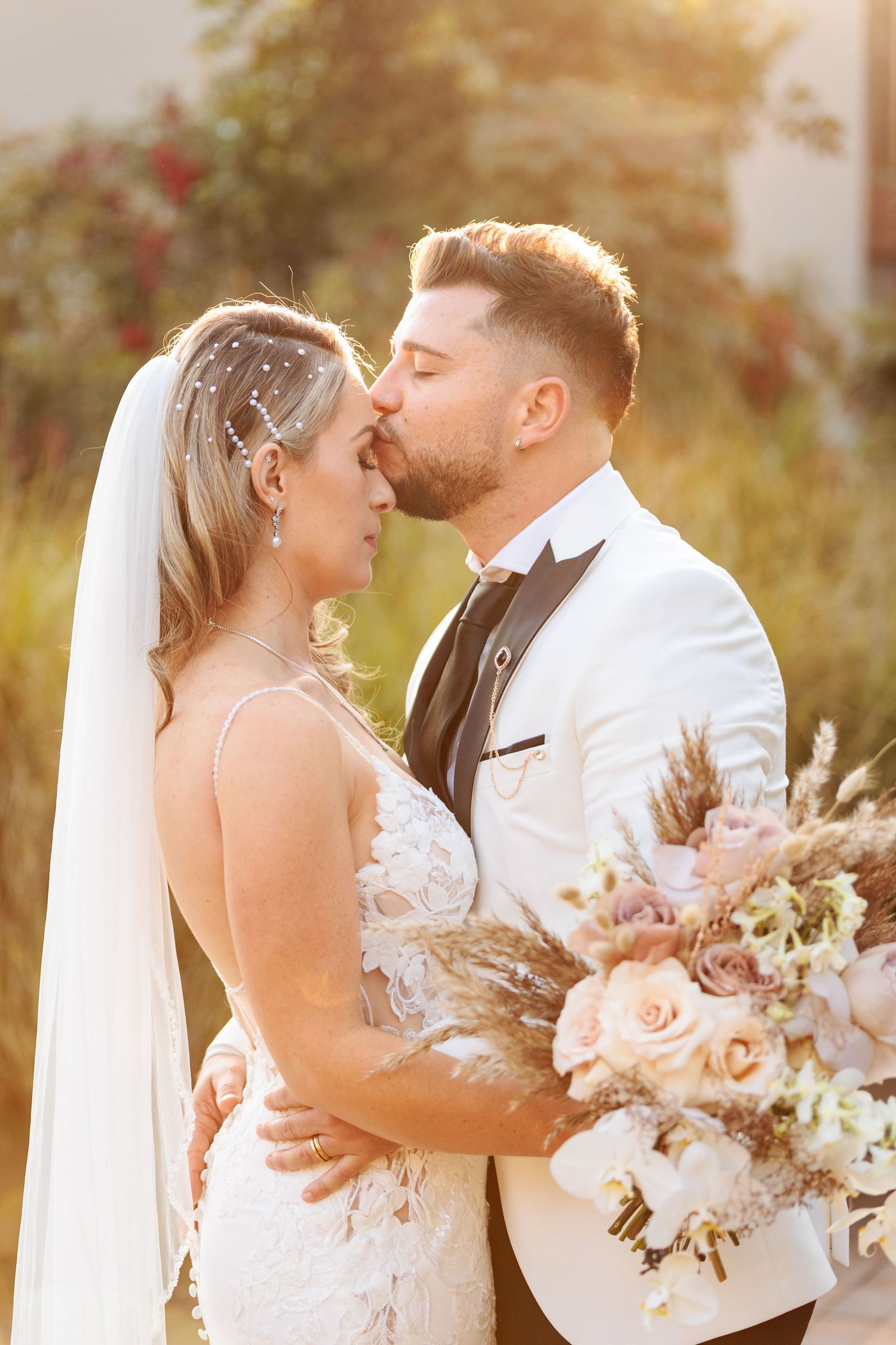 Romantic wedding couple embraces during golden hour sunset with blush and cream floral bouquet.