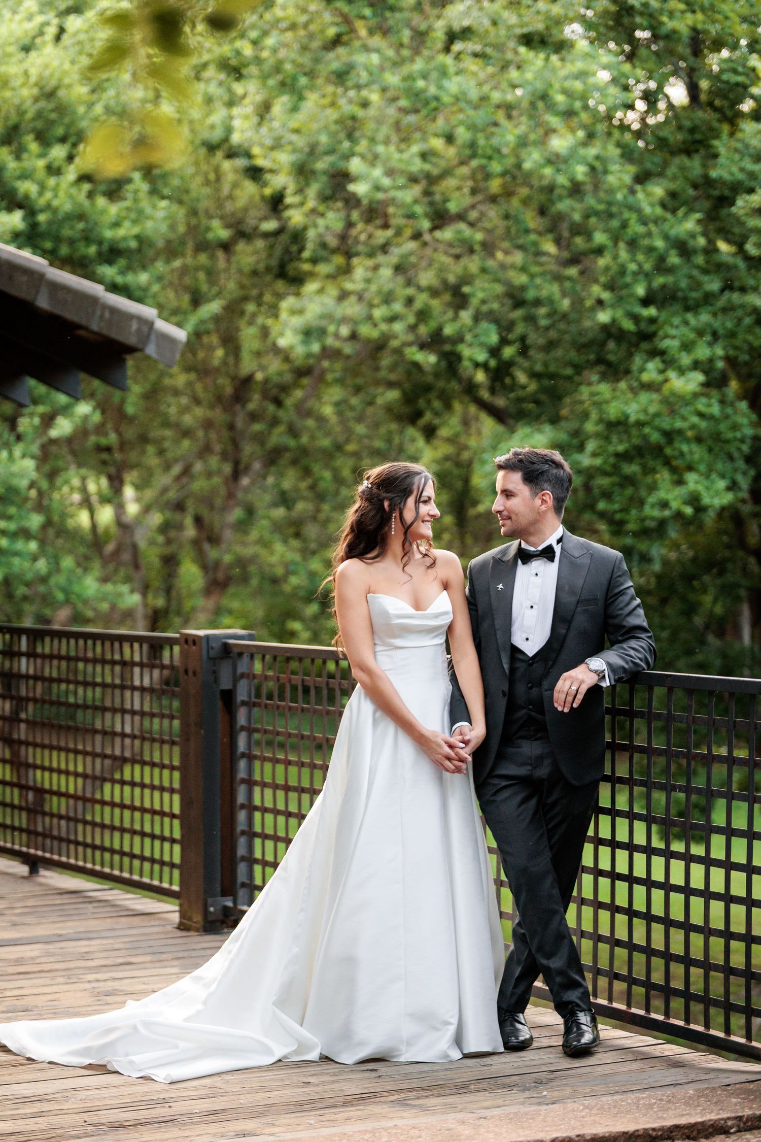 A couple shares romantic moments on a wooden deck surrounded by lush greenery during their wedding photoshoot.