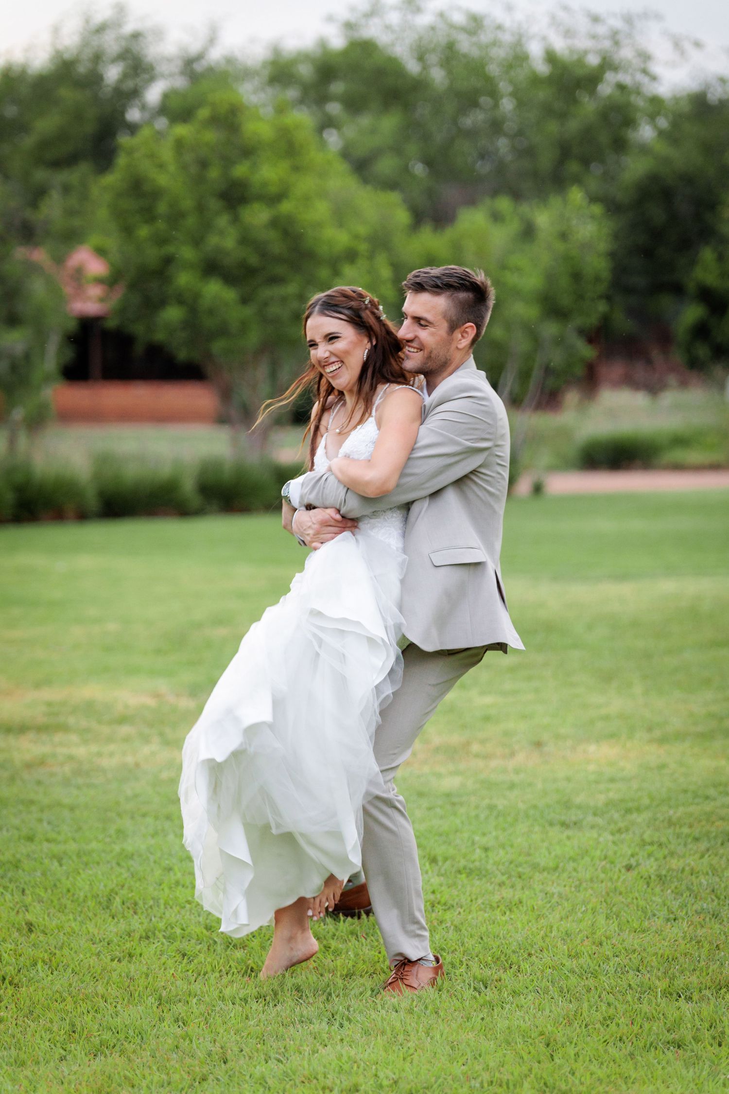 A playful wedding couple dances and spins on a grassy lawn during their celebration.