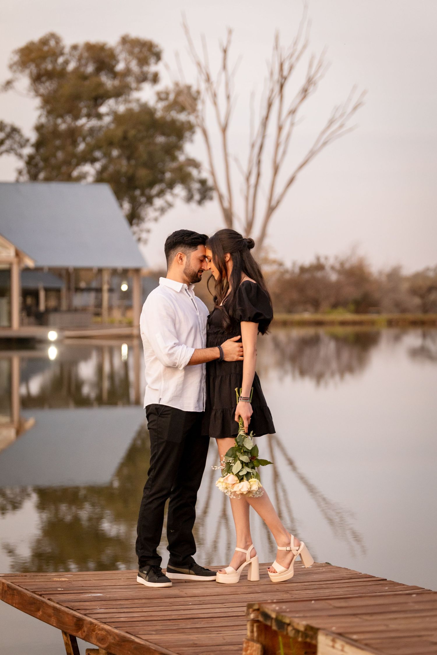 Romantic couple shares tender moments on a wooden dock by a serene lake at sunset.