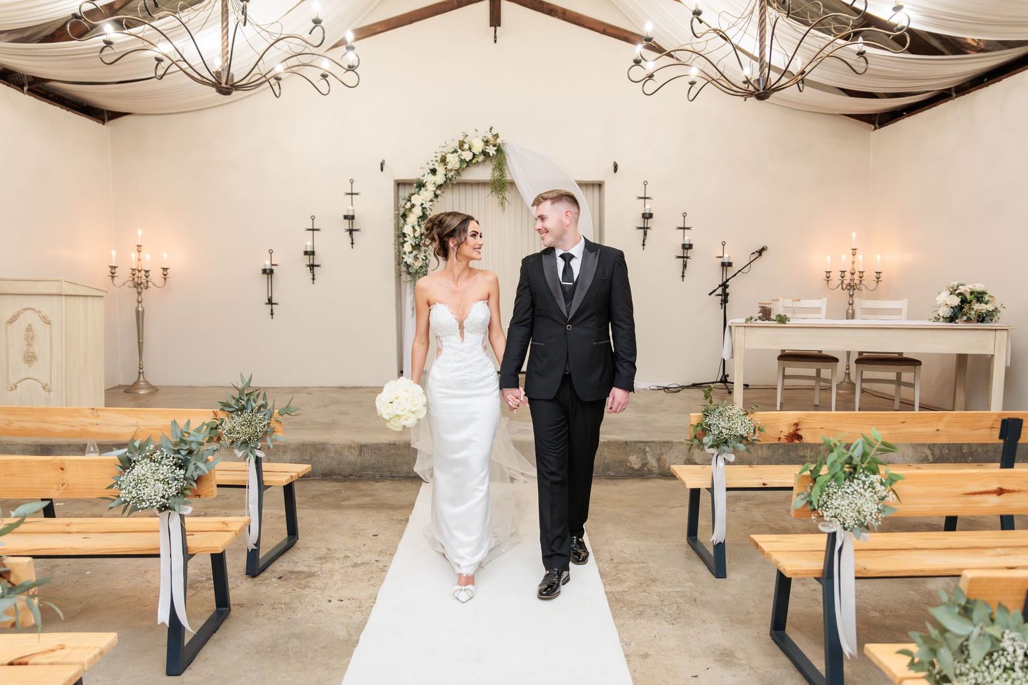 A rustic church venue features wooden pews, exposed beams, and elegant chandeliers for a wedding ceremony.